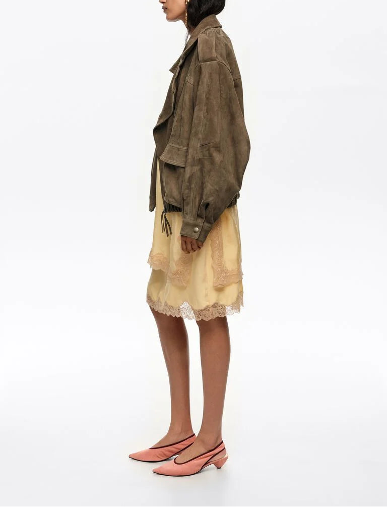 אישה לובשת ז׳קט חום מחויט, שמלת תחרה בהירה ונעלי בלט ורודות