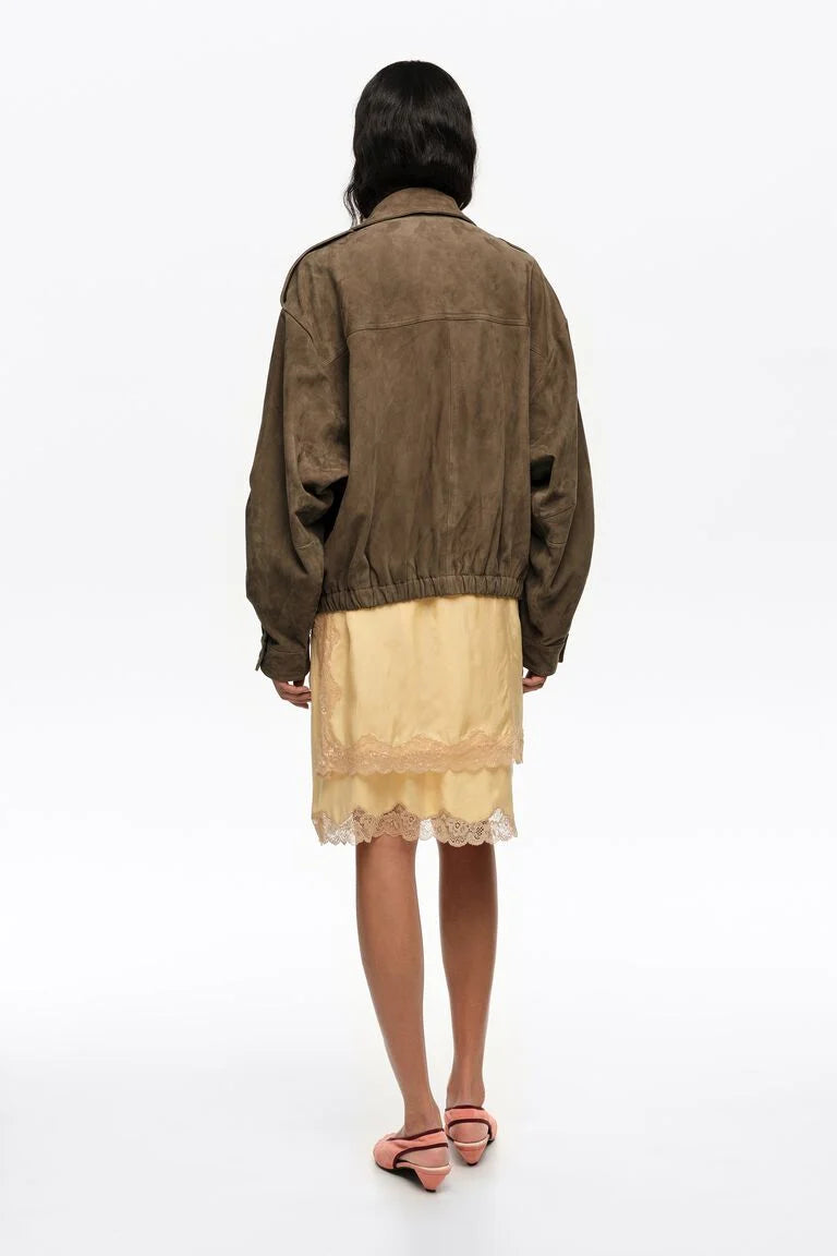 אישה עם ז'קט חום ומעל שמלה צהובה עם תחרה, נעלי עקב ורודות, צילום מגב על רקע לבן