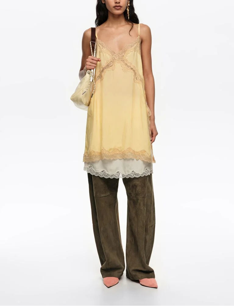 אישה לובשת שמלת תחרה צהובה עם כתפיות דקות מעל מכנסיים רחבים ירוקים ונעלי עקב ורודות