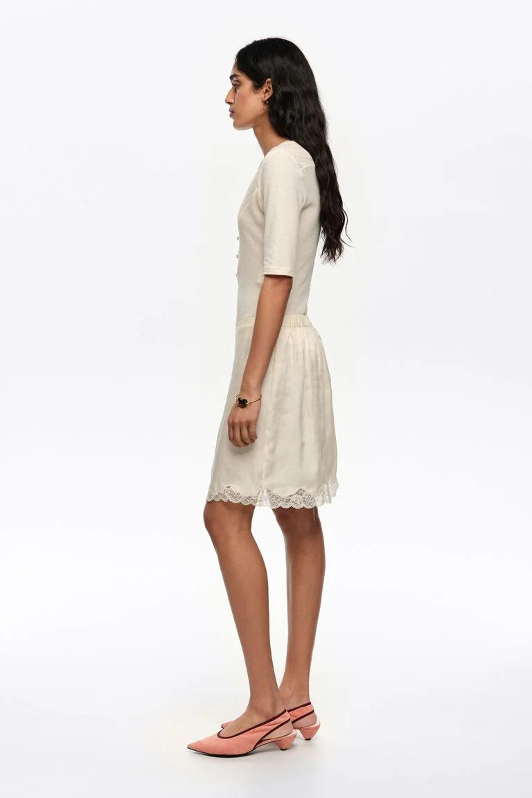 אישה לובשת שמלת קיץ בהירה עם שרוולים קצרים ותחרה בקצה, נעלי עקב ורודות