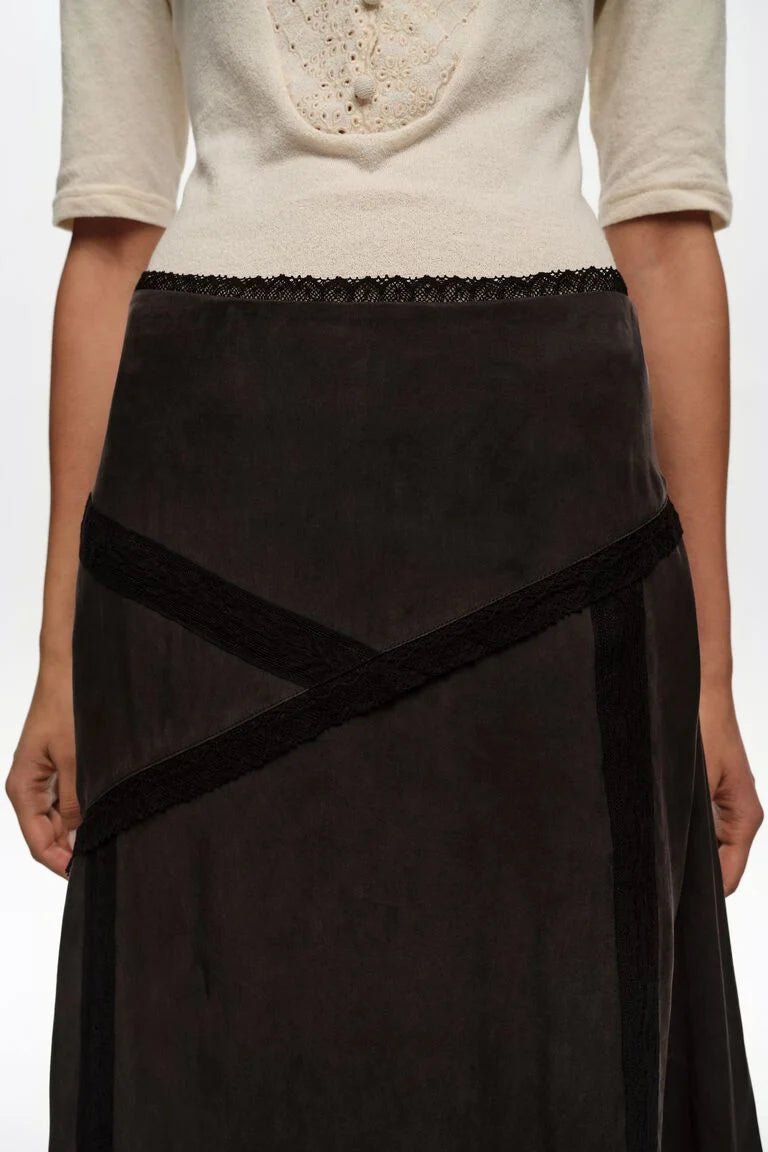 חצאית נשים שחורה עם פסי בד דקורטיביים, חולצת כפתורים בצבע שמנת, צילום אופנה על דוגמנית