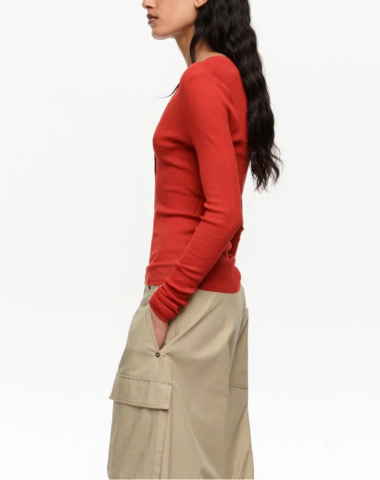 אישה עם סוודר אדום ומכנסי קארגו בז', מבט מהצד על רקע לבן