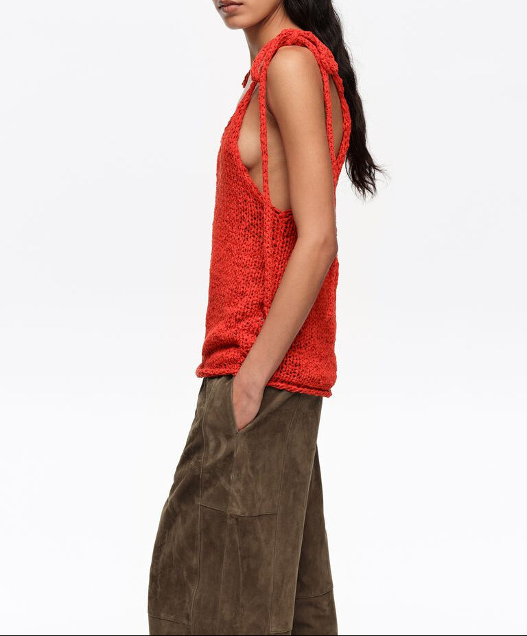 אישה עם גופיית סרוגה אדומה עם כתפיות קשירה ומכנסיים ירוקים, מראה אופנתי מודרני