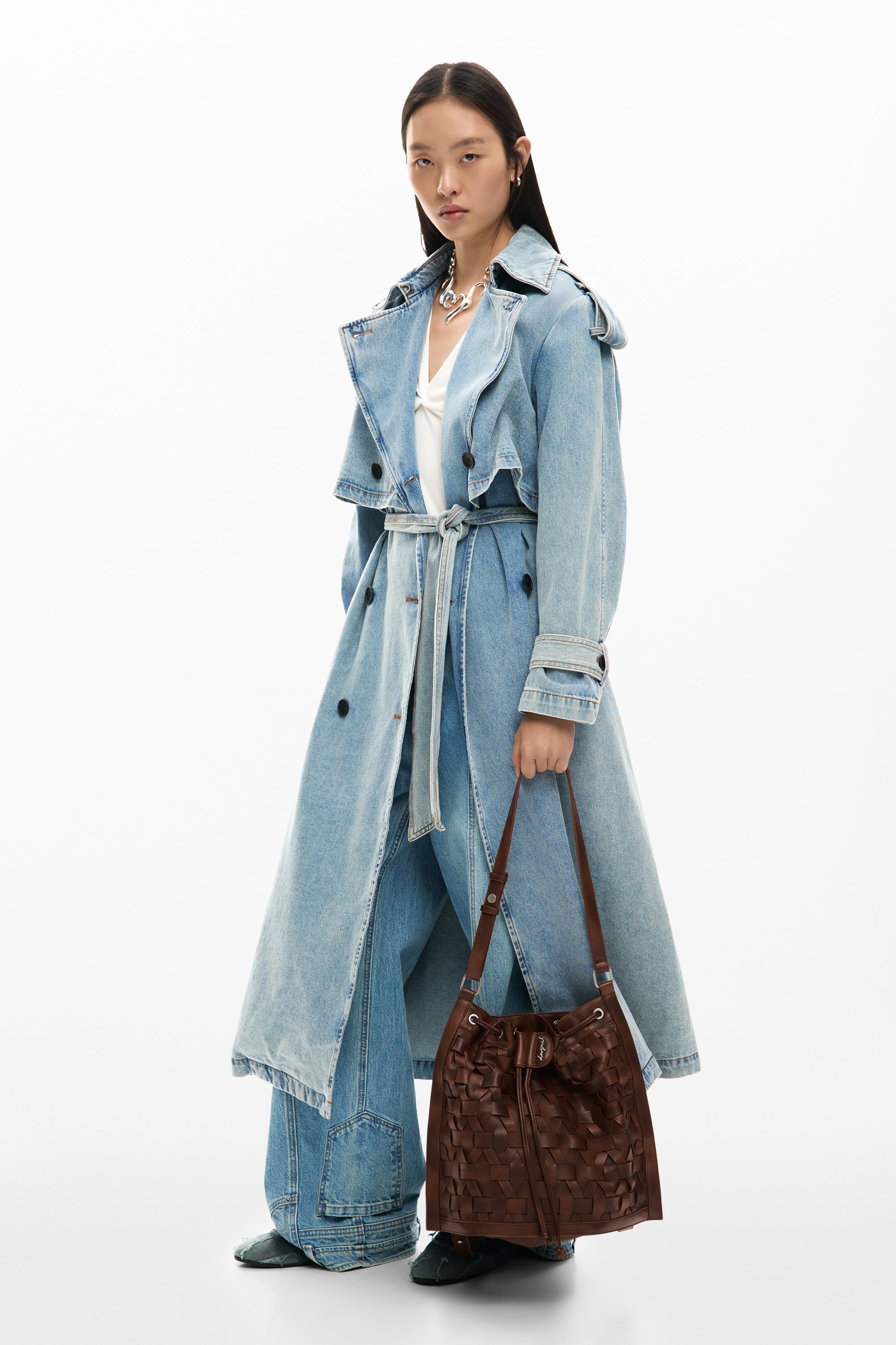 אישה עם מעיל ג'ינס ארוך, מכנסי ג'ינס רחבים ותיק יד חום קלוע, אופנה עכשווית