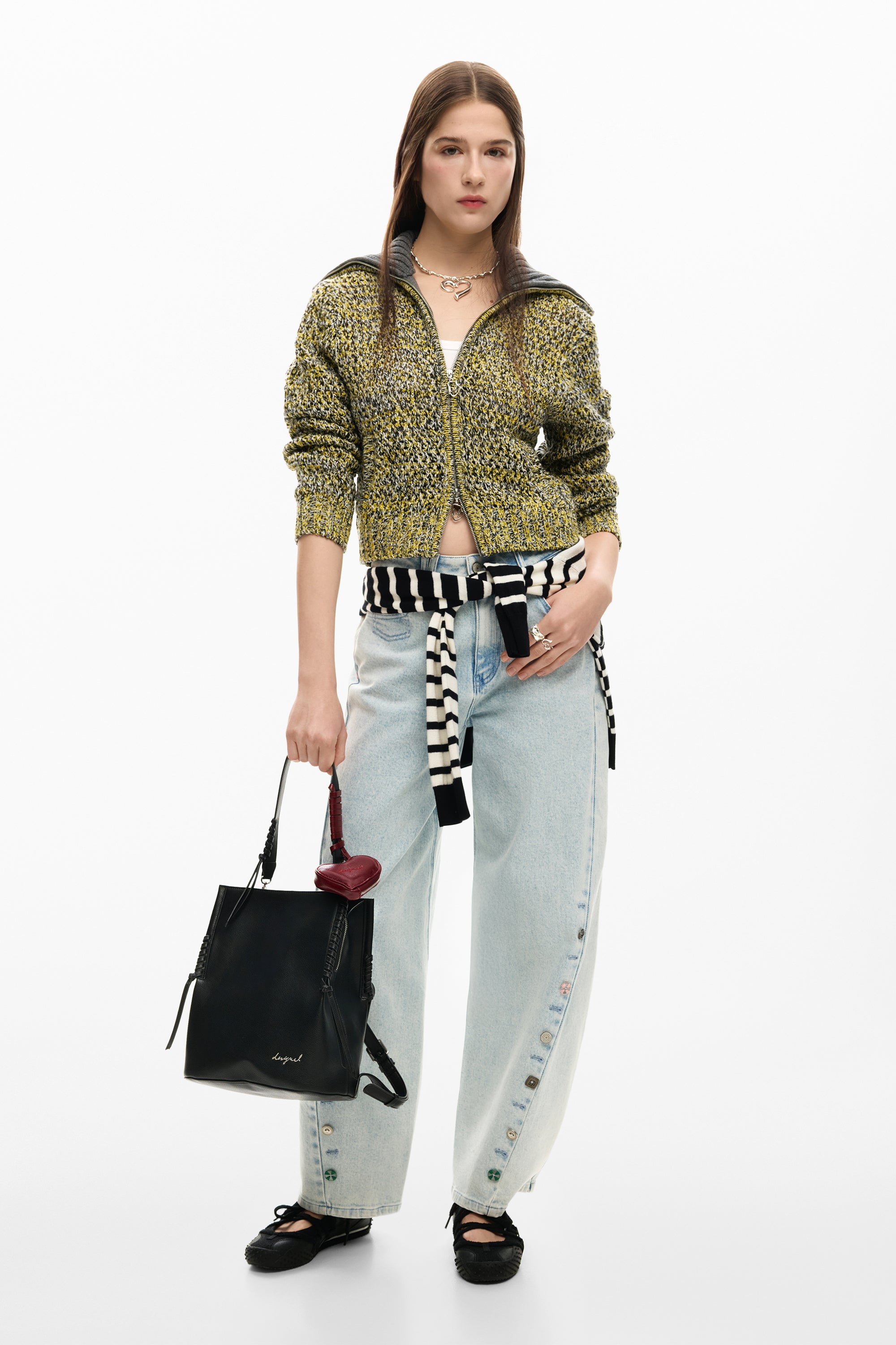 אישה עם סוודר צהוב סרוג, מכנסי ג'ינס רחבים עם כפתורים, תיק שחור ונעלי בובה.