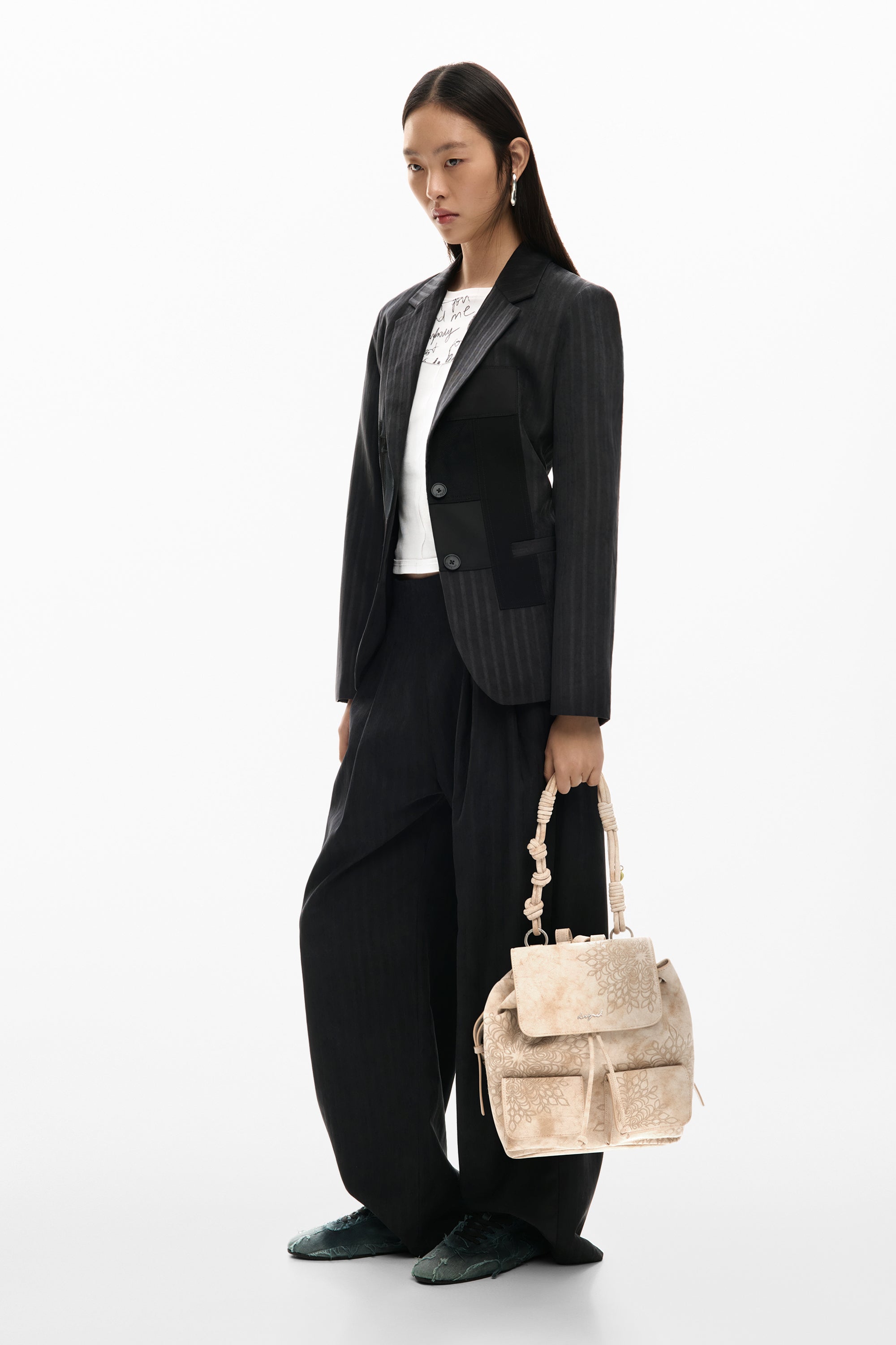 דוגמנית לובשת חליפת מכנסיים מחויטת שחורה, מחזיקה תיק יד בז' עם דוגמה פרחונית אופנתית