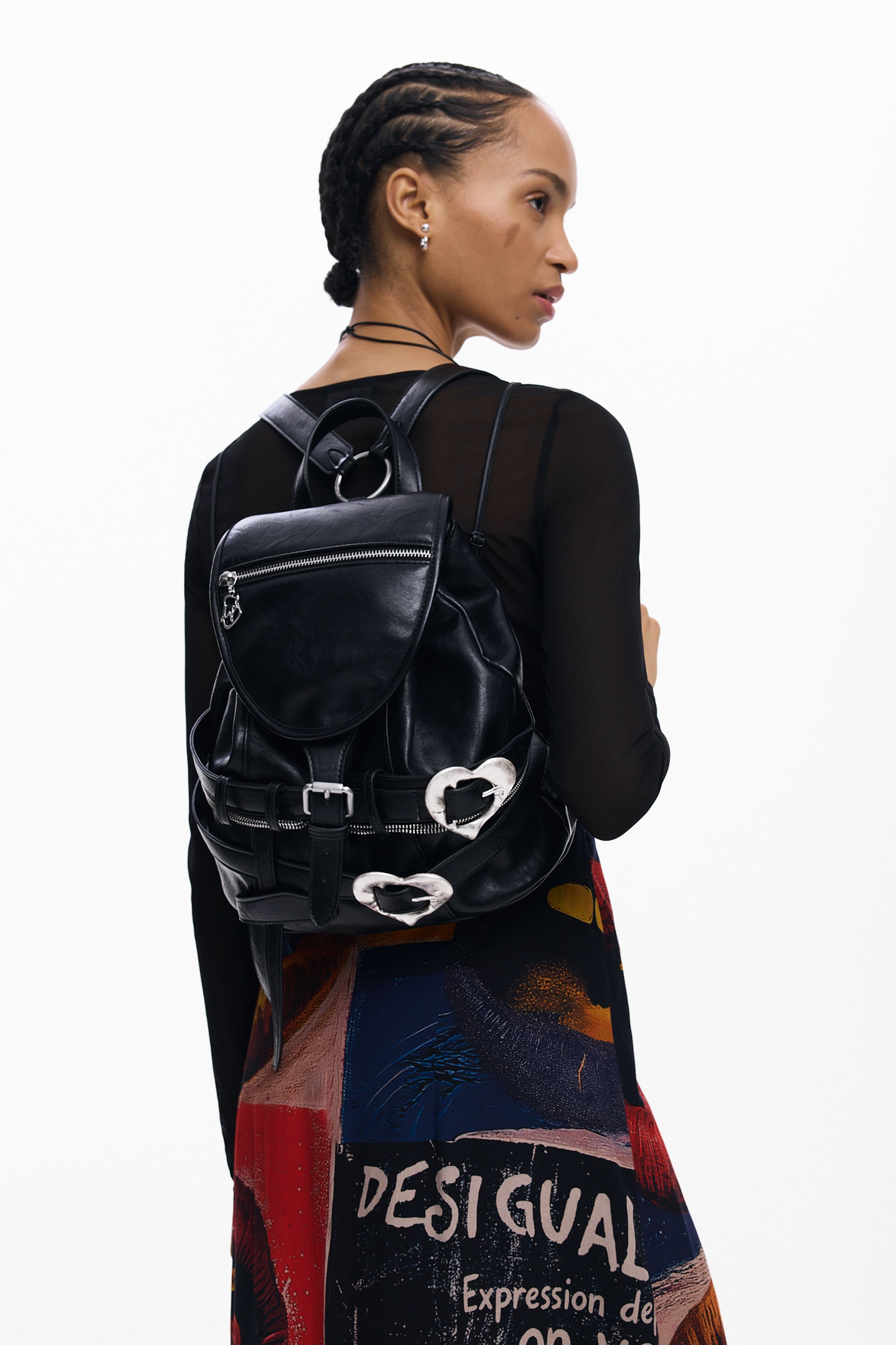 אישה עם תרמיל גב שחור עם אבזמי לב כסף, לובשת שמלה צבעונית עם כיתוב