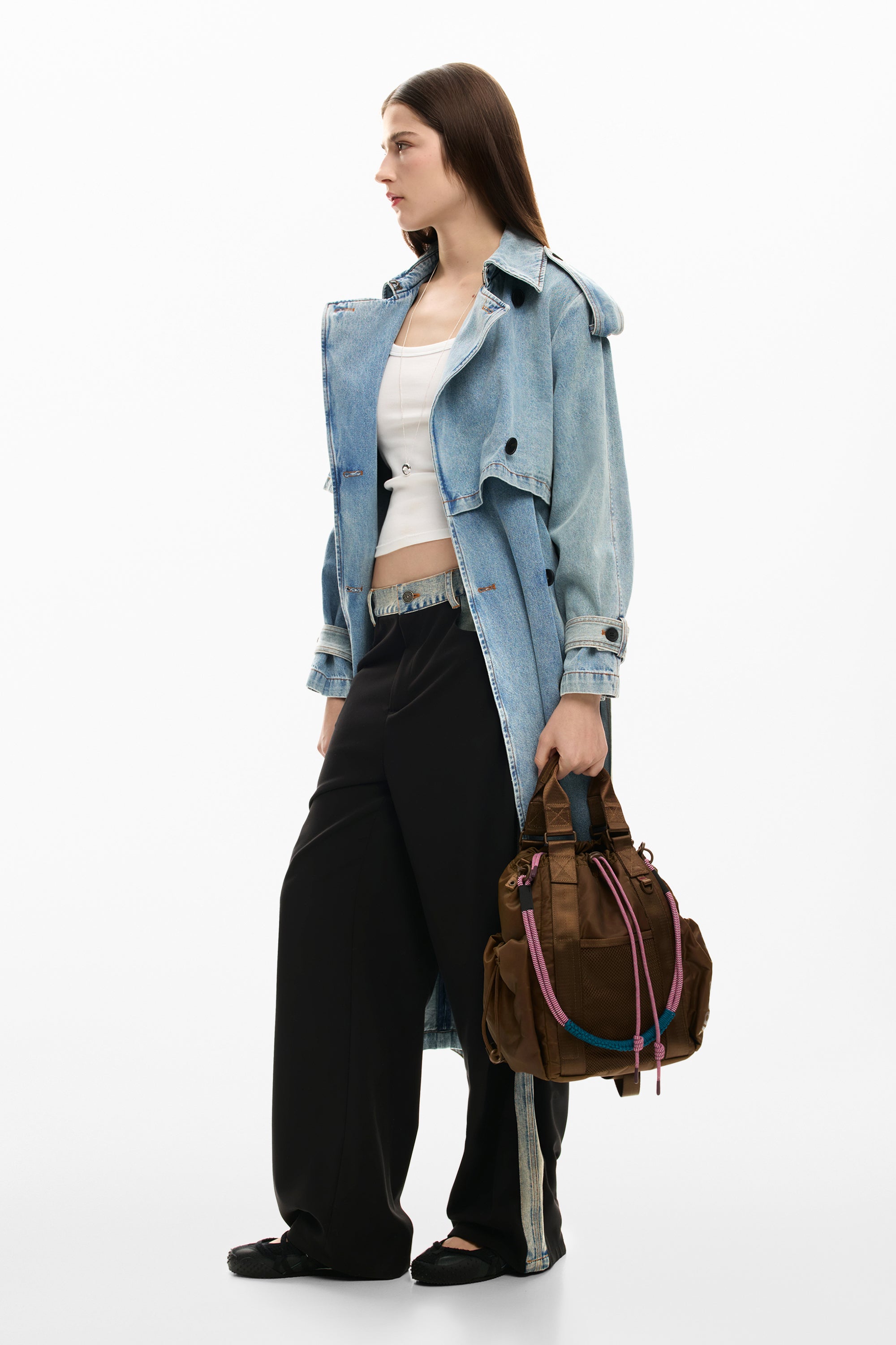 אישה עם מעיל ג'ינס, גופיה לבנה, מכנסיים רחבים ותיק יד חום עם חבלי צבע.