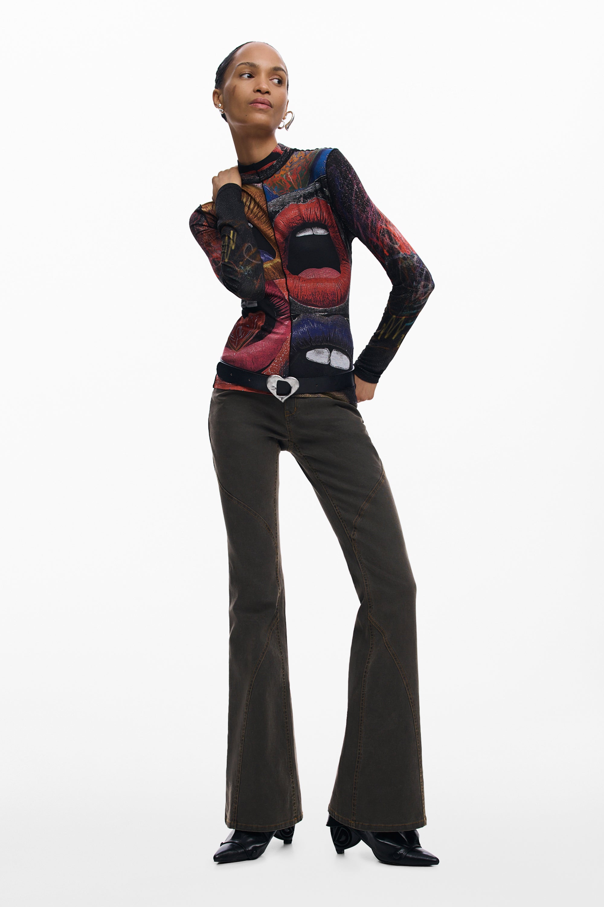 אישה לובשת חולצה צבעונית עם הדפס שפתיים, מכנסיים כהים ומגפיים על רקע לבן