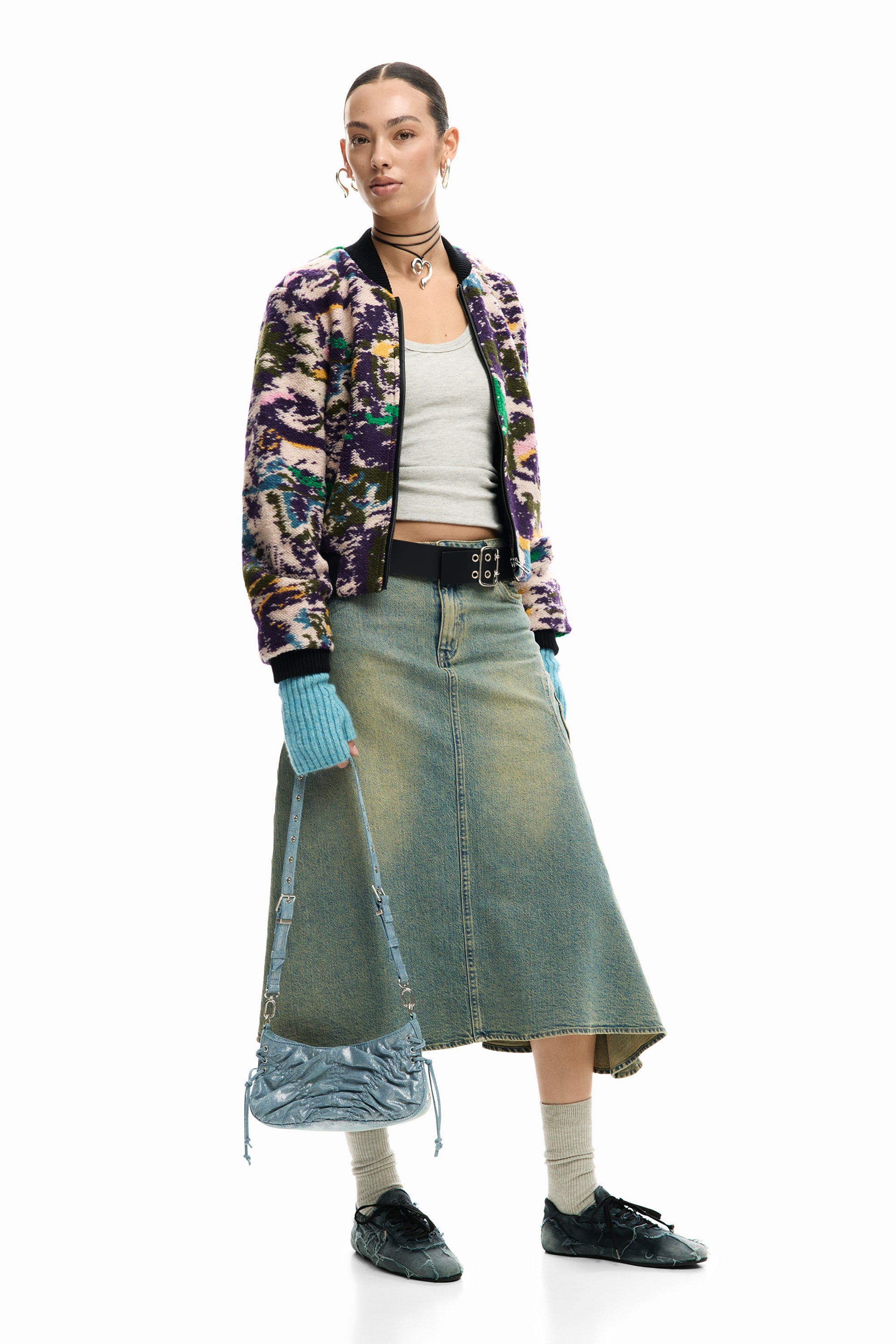 אישה לובשת ג'קט צבעוני, גופיה אפורה, חצאית ג'ינס ארוכה, כפפות כחולות, תיק צד ונעליים תואמות לאופנת רחוב.