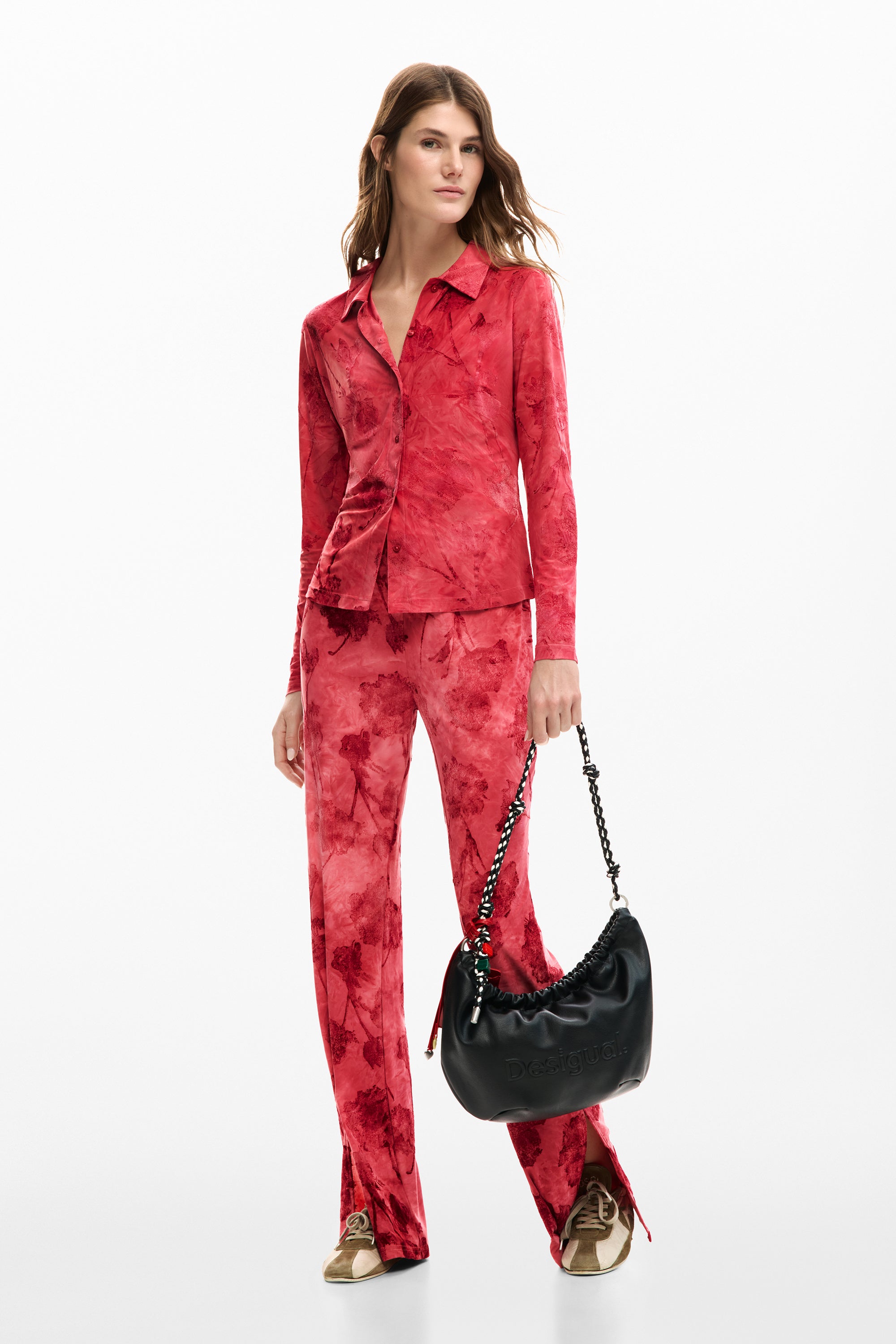 אישה בלבוש אופנתי חליפה אדומה עם דוגמה מופשטת, תיק צד שחור ונעלי סניקרס