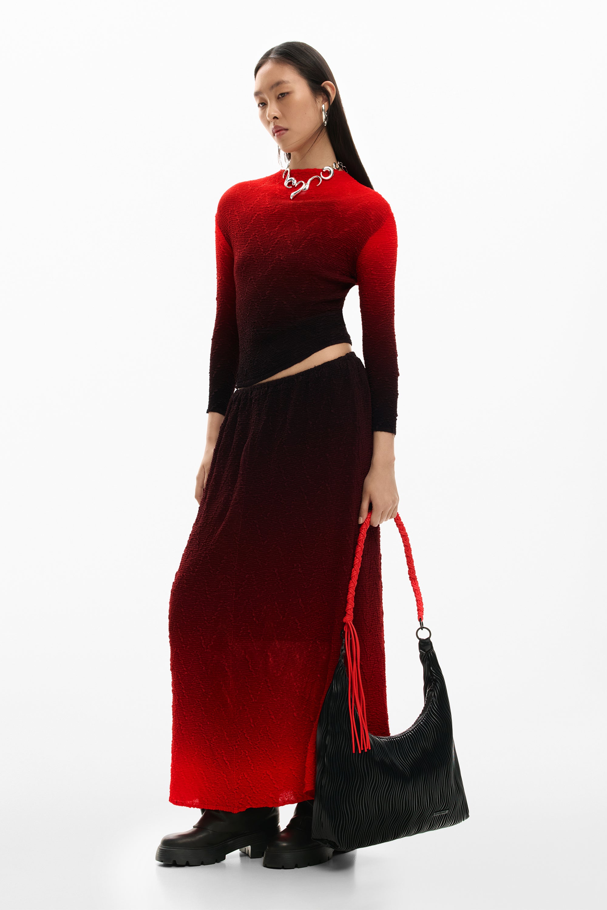 דוגמנית עם שמלה אדומה שחורה מכופתרת, תיק כתף שחור עם רצועה אדומה, מגפיים שחורים, רקע לבן