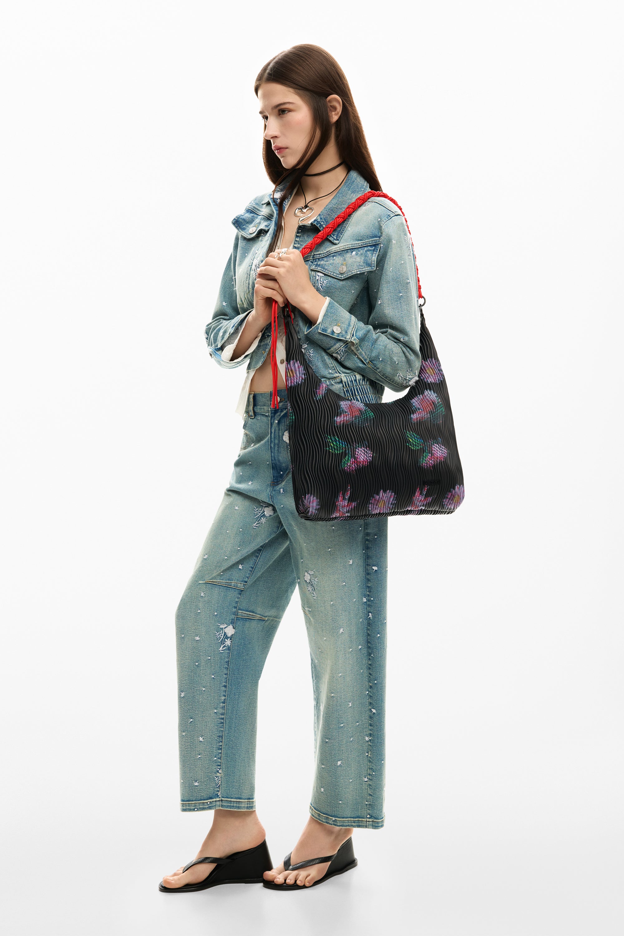 אישה עם ז'קט ג'ינס ותיק בד שחור עם הדפס פרחים צבעוני, סנדלים שחורים, מראה אופנתי