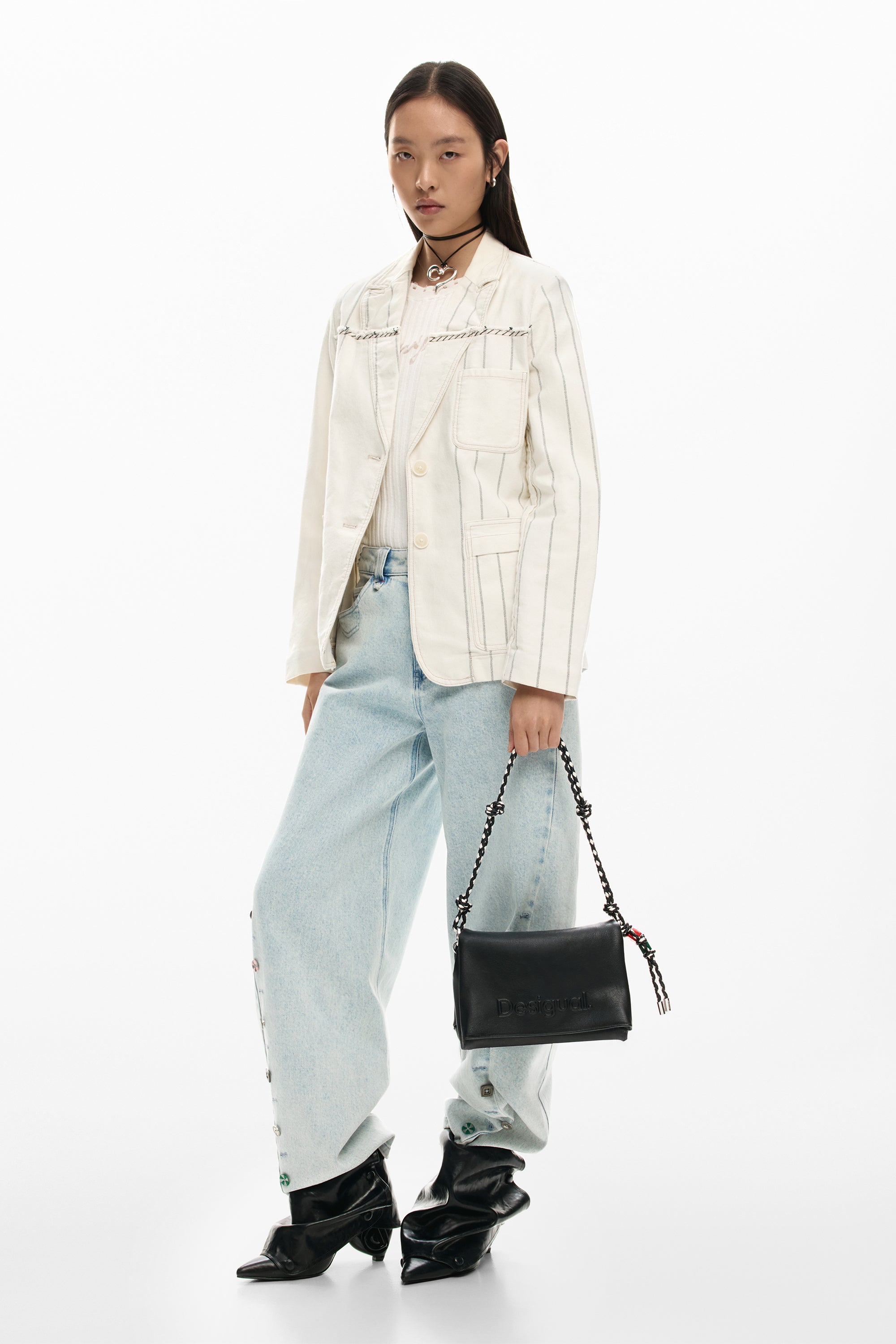 אישה עם ז'קט פסים לבן, מכנסי ג'ינס רחבים, נעלי עקב שחורות ותיק יד שחור לאופנת רחוב