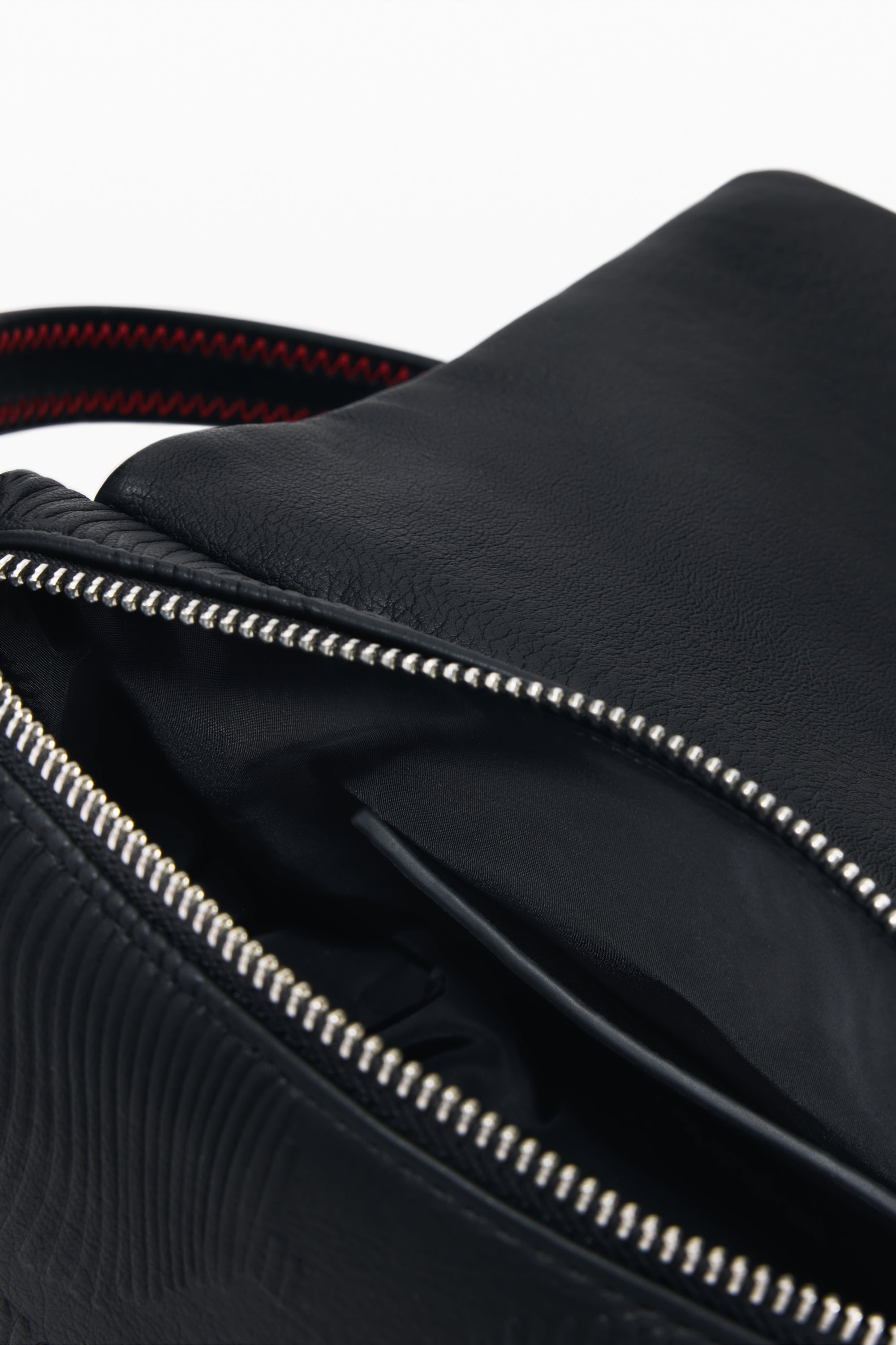 תקריב על תיק צד עור שחור, רוכסן פתוח ותפר אדום ברצועה