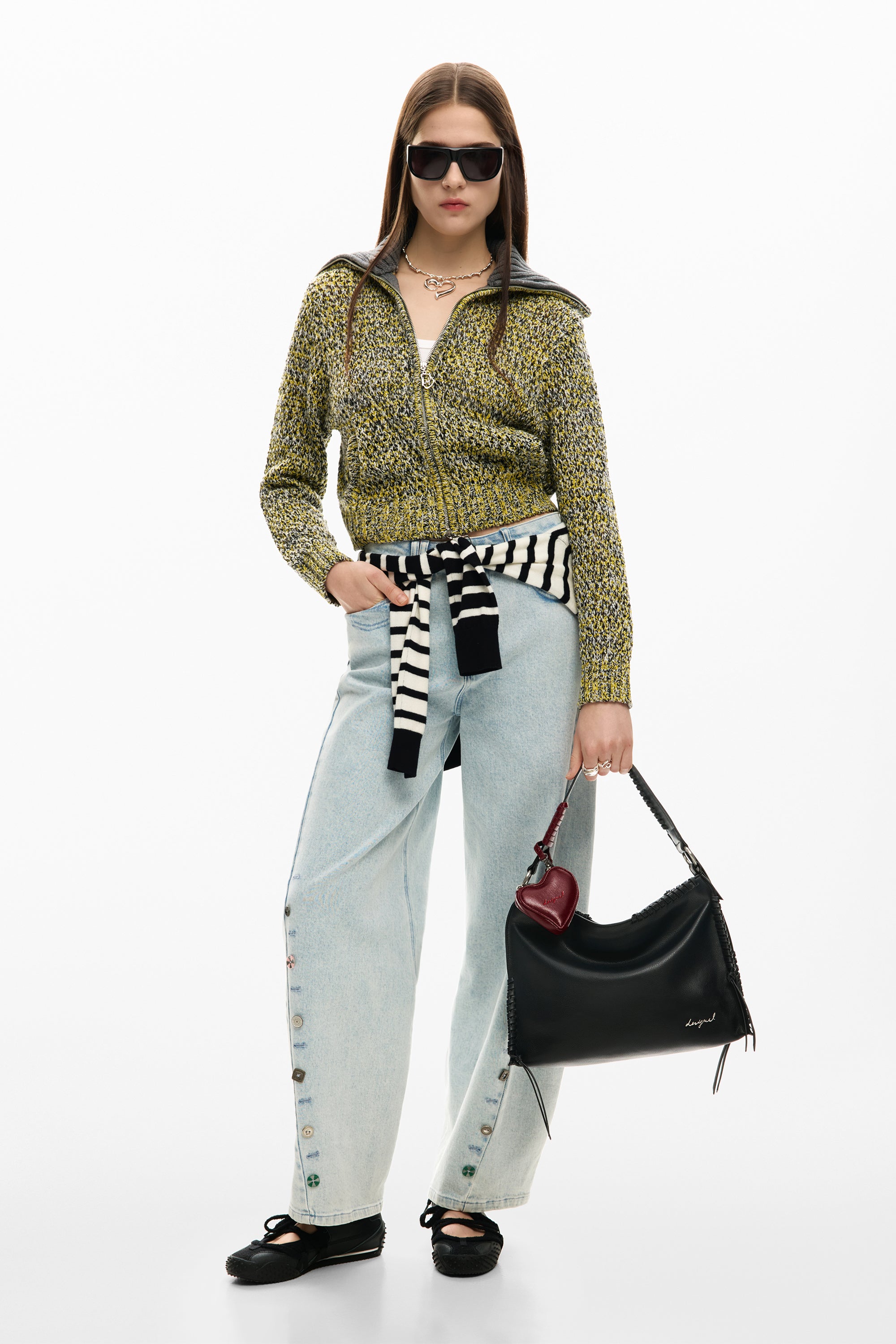 אישה עם סוודר צהוב-שחור, ג'ינס רחב, משקפי שמש ותיק עור שחור אופנתי