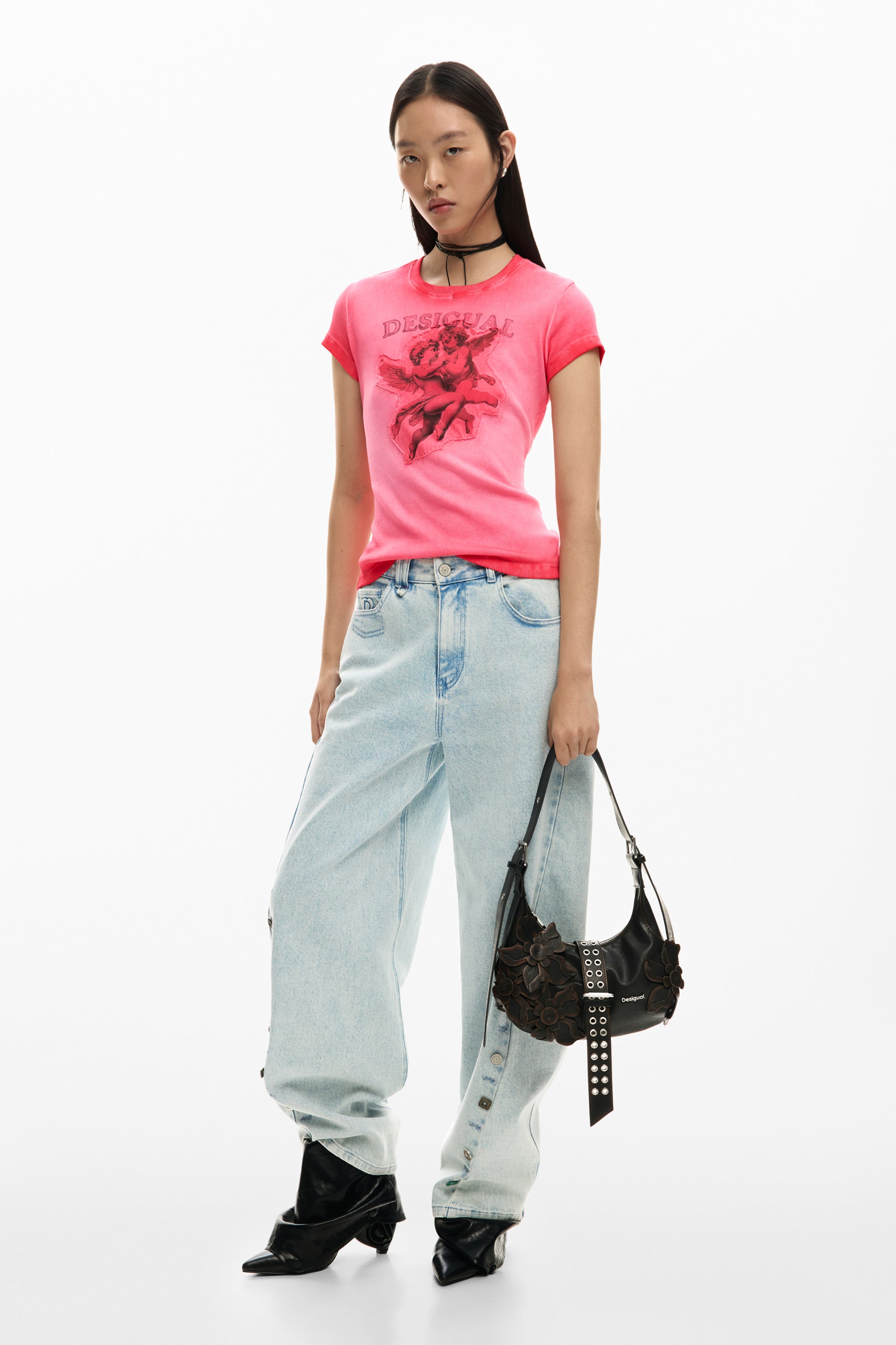 אישה לובשת חולצת טי ורודה עם הדפס, ג'ינס רחב ותיק יד שחור עם עיטורי פרחים