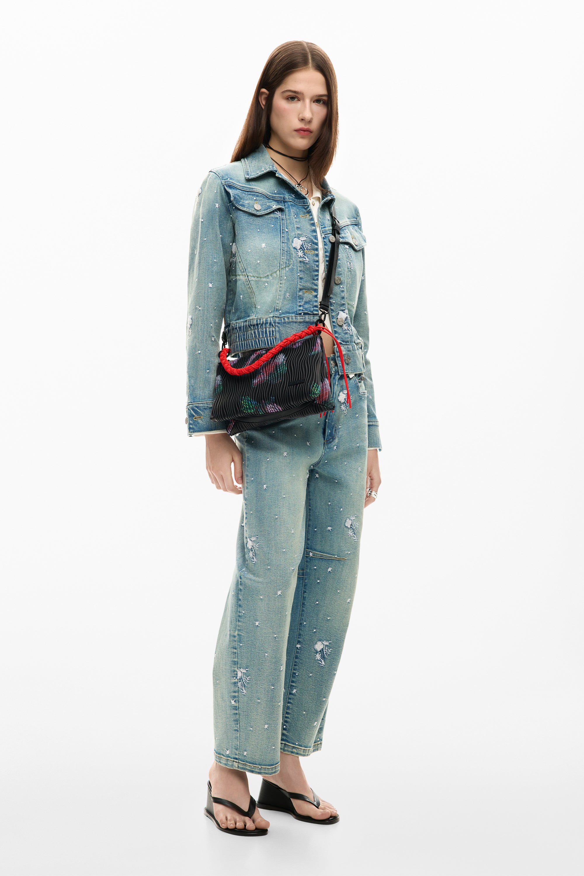 אישה לובשת חליפת ג'ינס משופשפת עם תיק צד שחור-אדום ועקבים שחורים, אופנת רחוב טרנדי