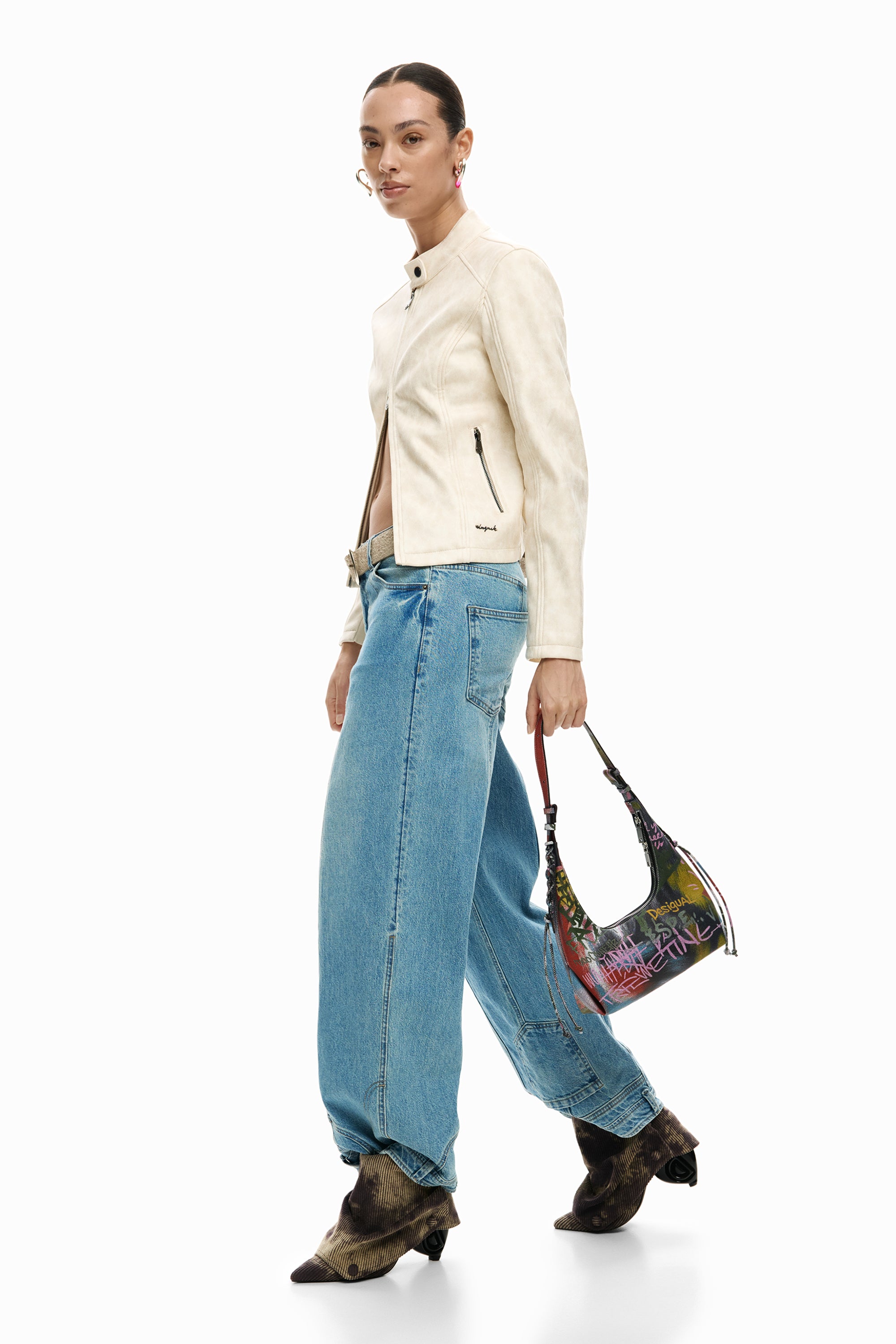 אישה עם ג'קט בהיר, ג'ינס רחב, מגפיים חומים ותיק צד קטן עם הדפס צבעוני