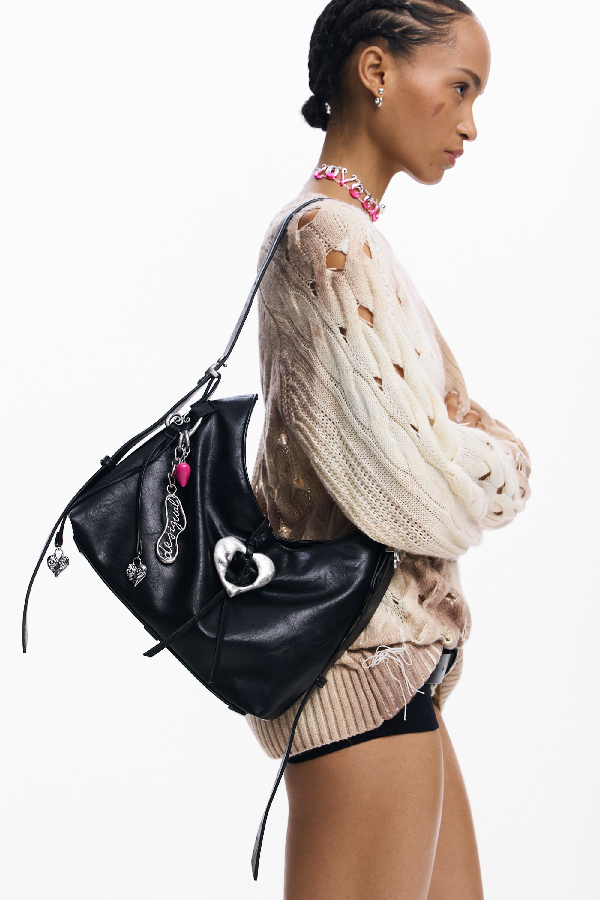 אישה עם סוודר קרם מחורר ותיק כתף שחור עם קישוטים בצורת לב ותליונים אופנתיים