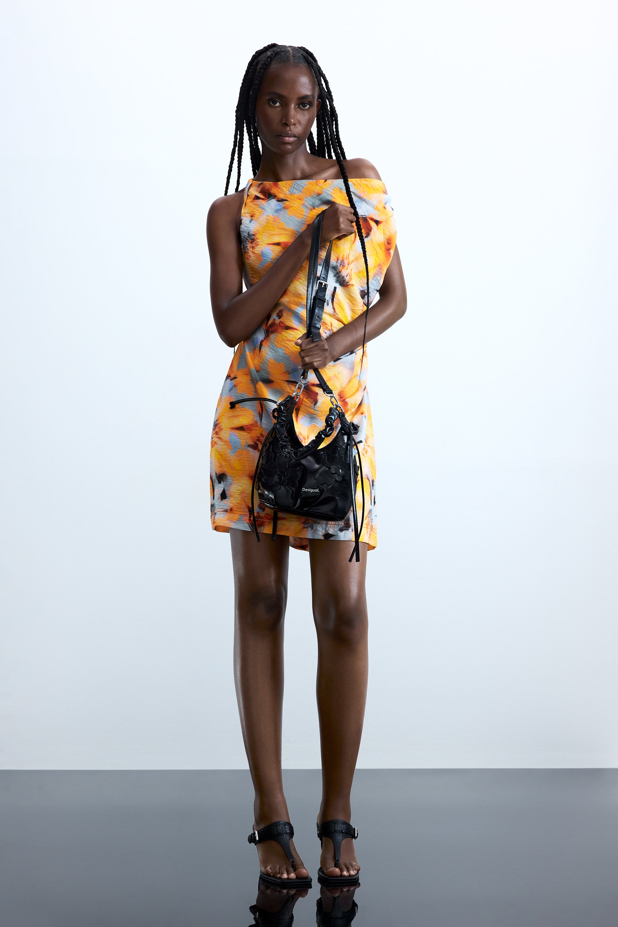 אישה בלבוש קיץ, שמלה צבעונית בהדפס צהוב-כתום ותיק שחור אופנתי, רקע לבן מינימליסטי