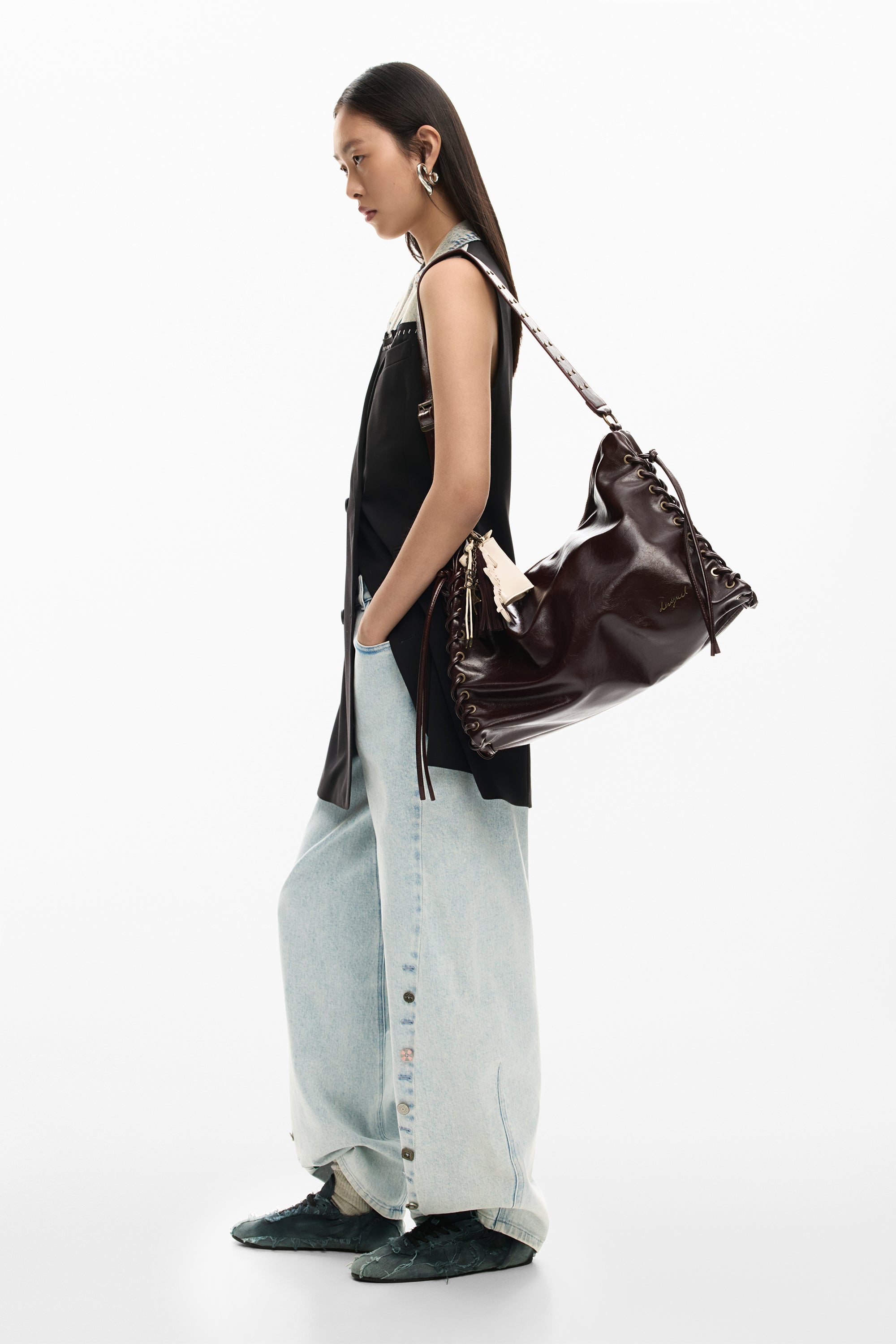 אישה עם תיק כתף מעור חום, חולצה שחורה ומכנסי ג'ינס רחבים אופנתיים על רקע לבן