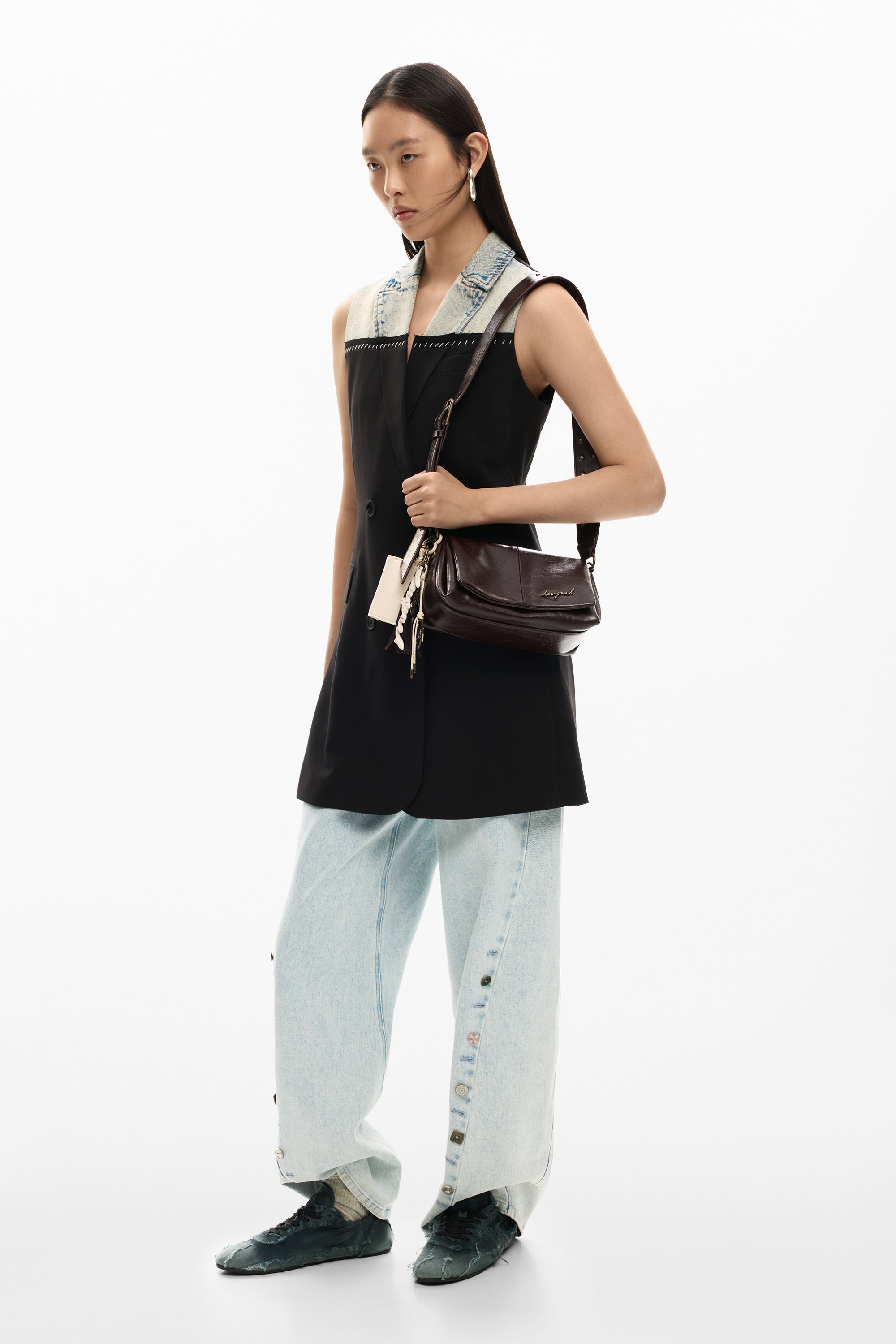 אישה לובשת ג'קט שחור עם צווארון דנים, מכנסי ג'ינס רחבים, נעלי סניקרס שחורות ותיק צד חום