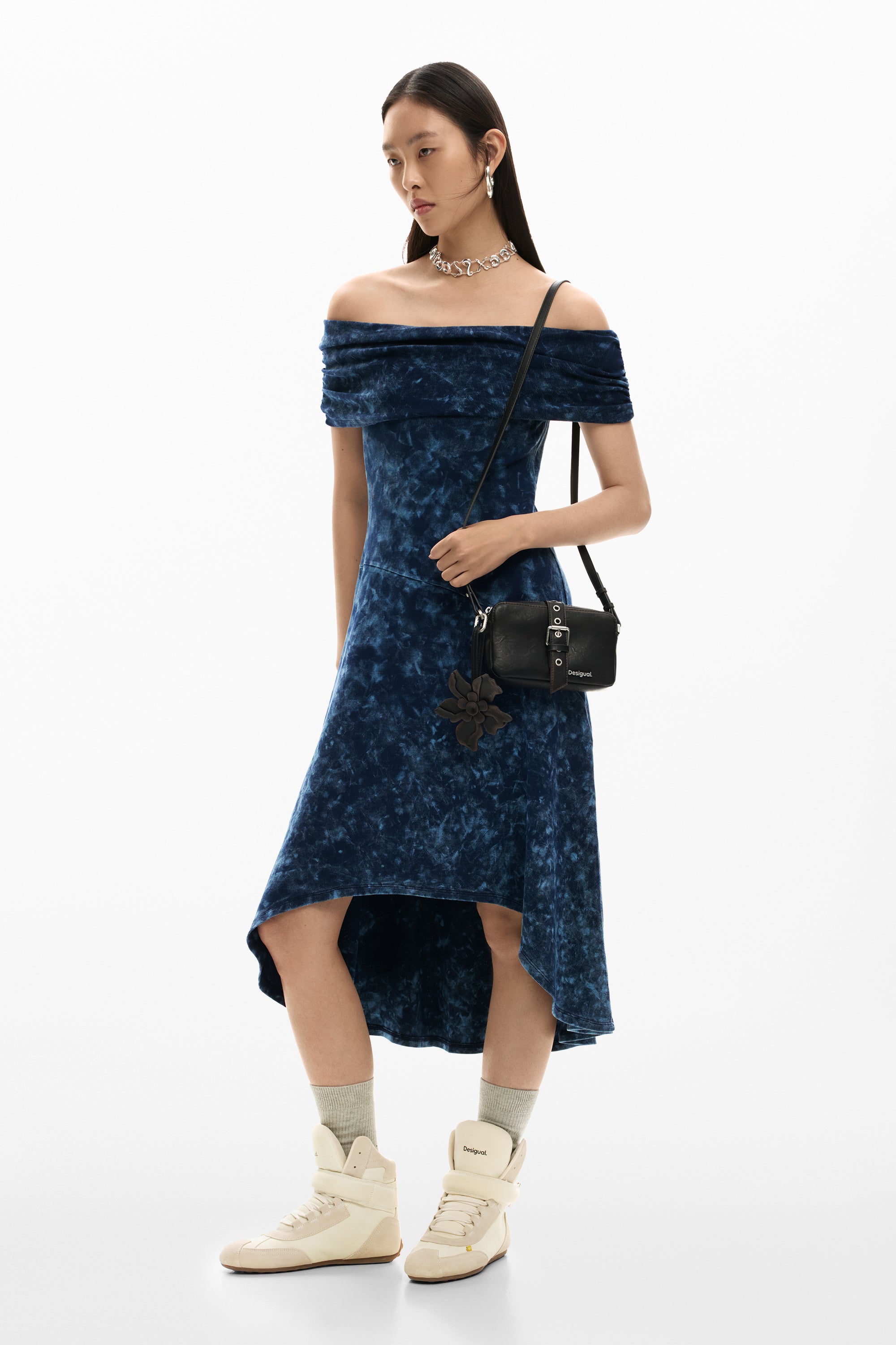 אישה עם שמלת כתפיים כחולה, תיק צד שחור ונעלי ספורט בז׳, סטייל אופנתי ואלגנטי