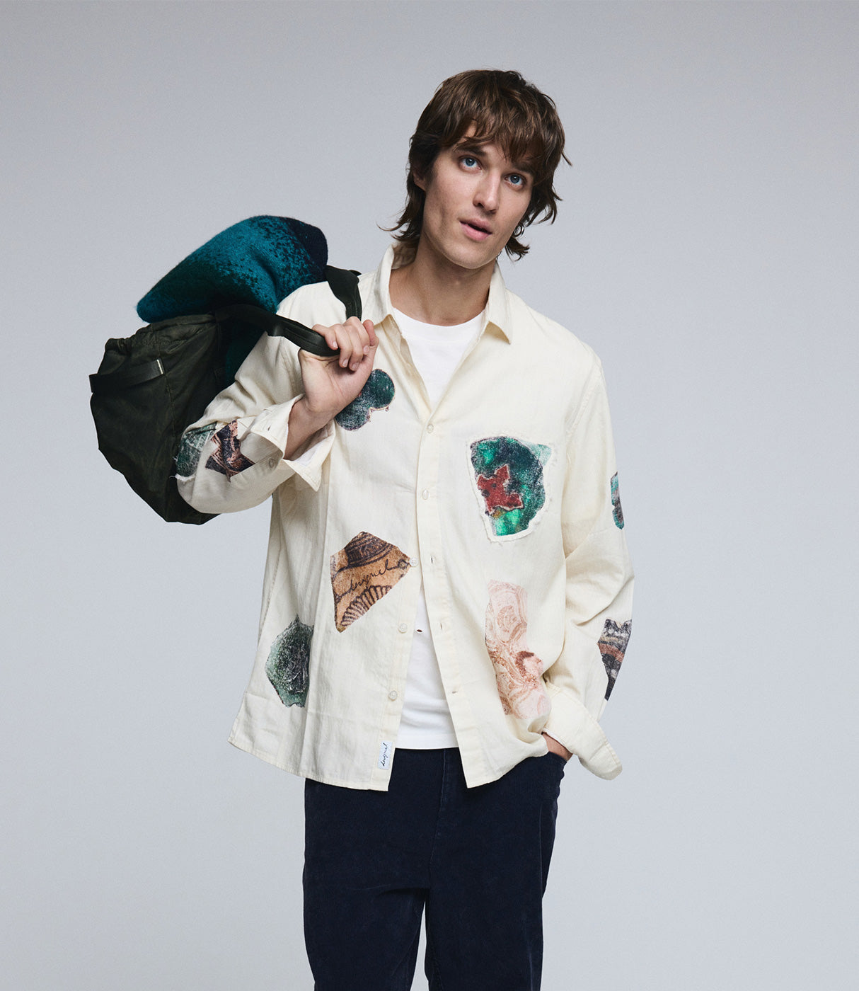 דוגמן עם חולצה לבנה מודפסת טלאים צבעוניים, מכנס כהה ותיק ירוק, צילום סטודיו לאופנה