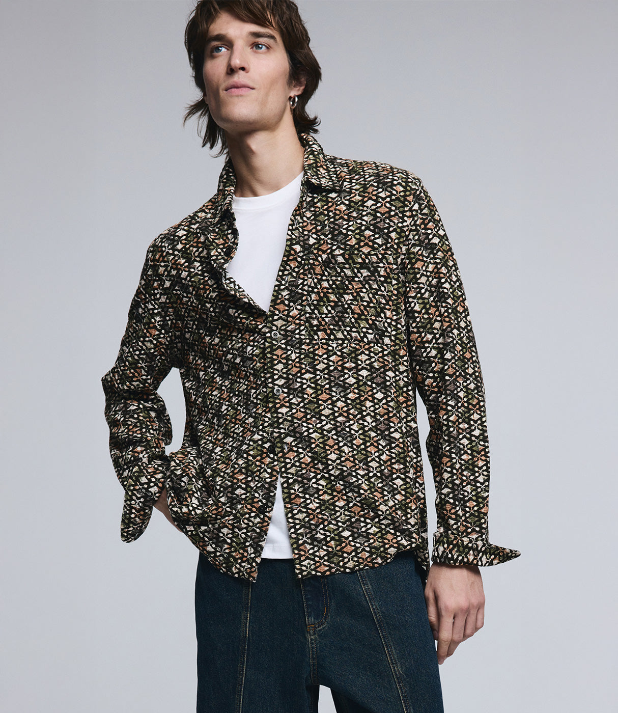 גבר עם חולצה מכופתרת מודפסת בגווני שחור וחום, חולצת בסיס לבנה ומכנסי ג'ינס