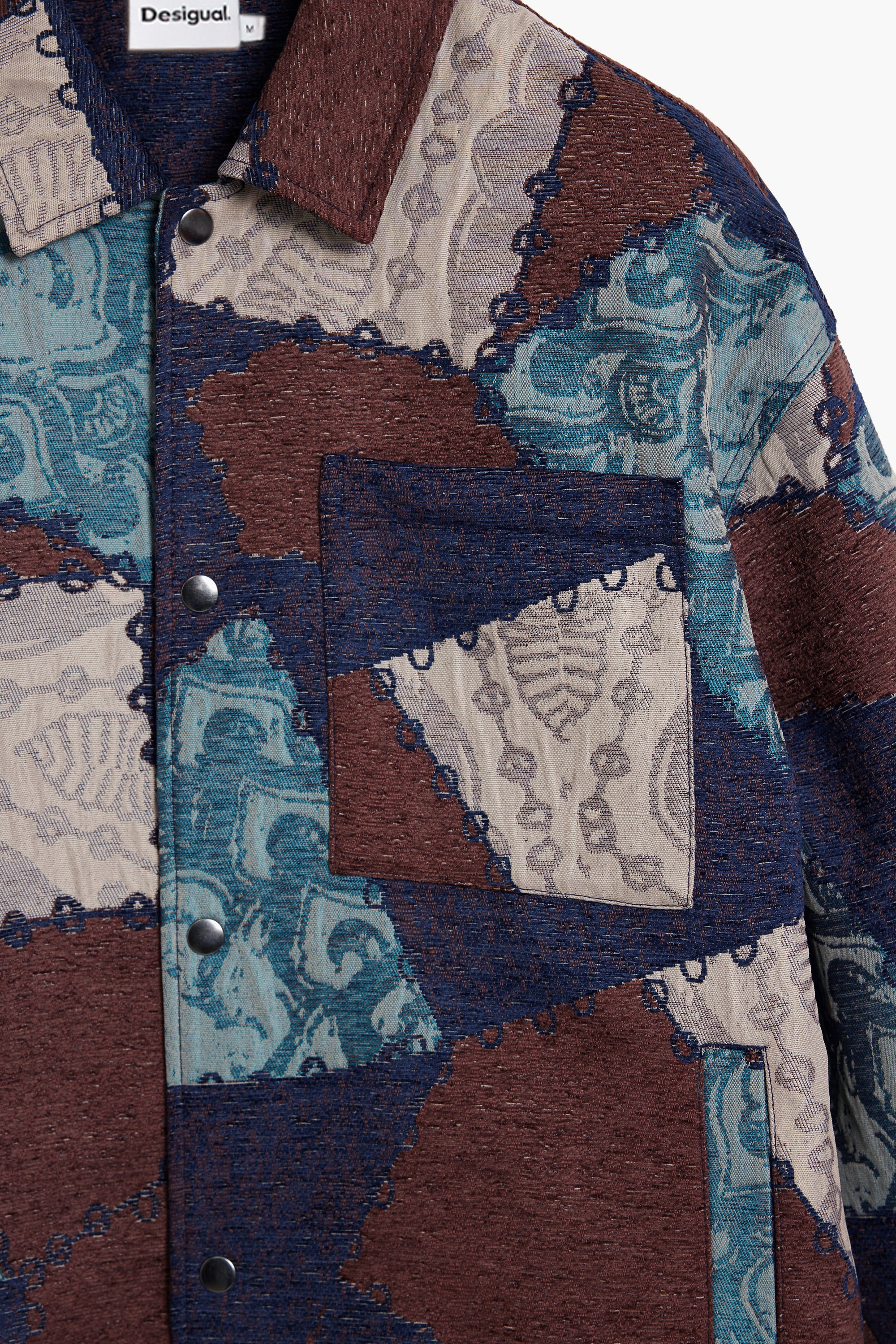 חולצה בגזרת ג'קט בדוגמת בלוקי טלאים בצבעי כחול, חום ובז' עם כיס קדמי וכפתורים.