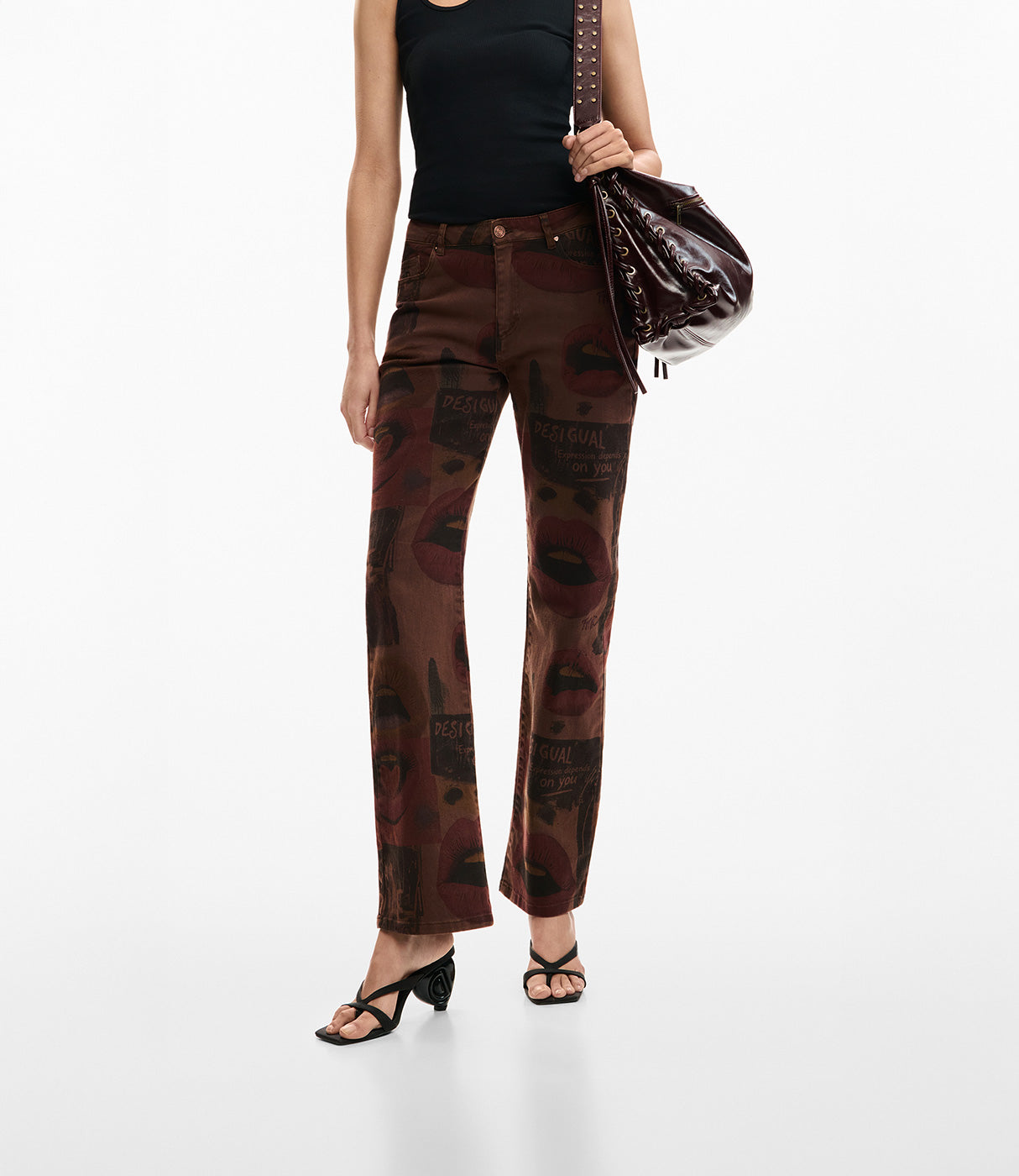 אישה לובשת מכנסיים חומים מודפסים בדוגמת שפתיים עם גופיה שחורה ונעליים פתוחות