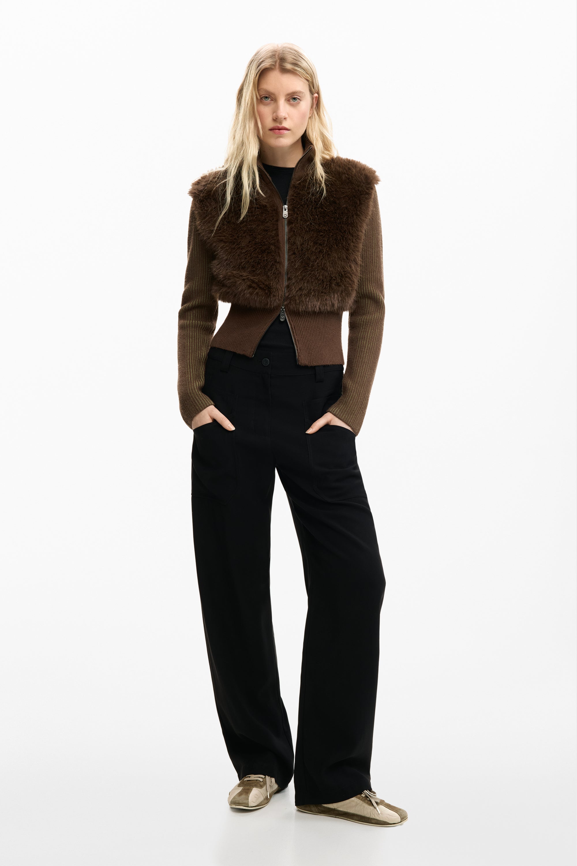 דוגמנית לובשת סוודר חום עם פרווה מלאכותית, מכנסיים רחבים שחורים ונעלי ספורט אופנתיות