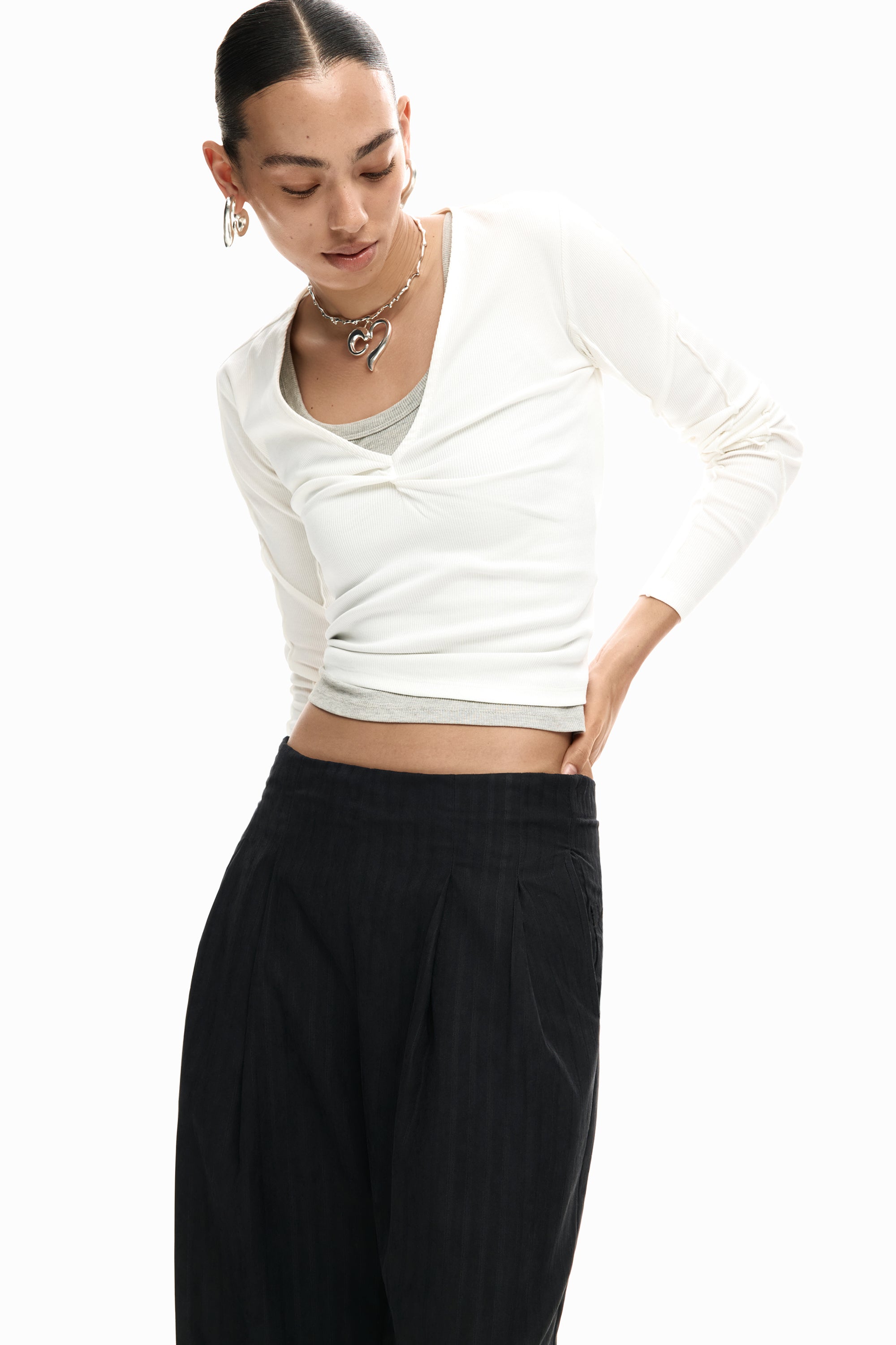 אישה לובשת חולצת וי לבנה עם שרוולים ארוכים, מכנסיים שחורים ותכשיטים אופנתיים