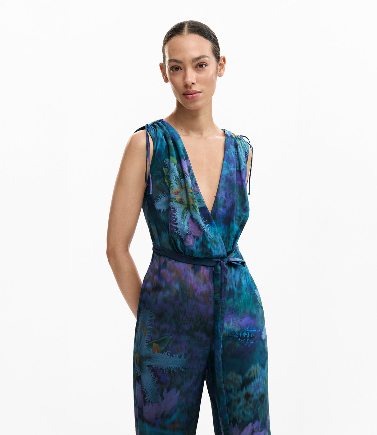 אישה לובשת אוברול בדוגמת פרחים בגווני כחול וסגול, מחשוף עמוק, חגורה במותן