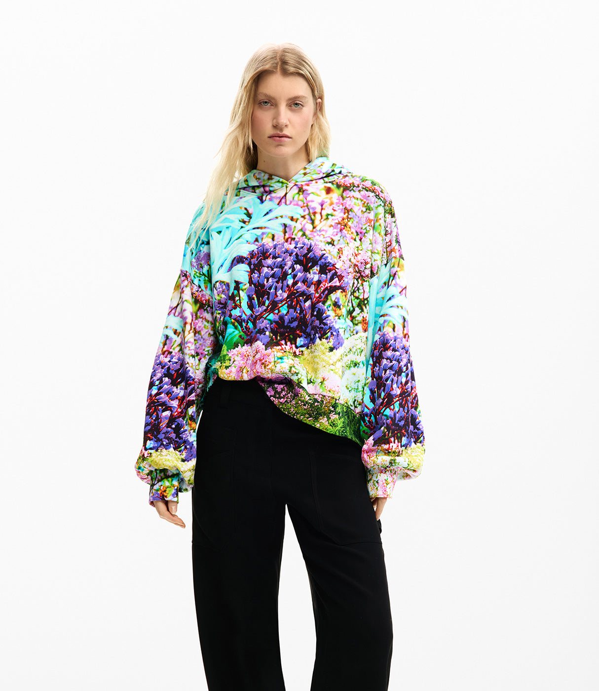 אישה לובשת קפוצ'ון צבעוני עם הדפס פרחים צבעוני, מכנסיים שחורים רקע לבן