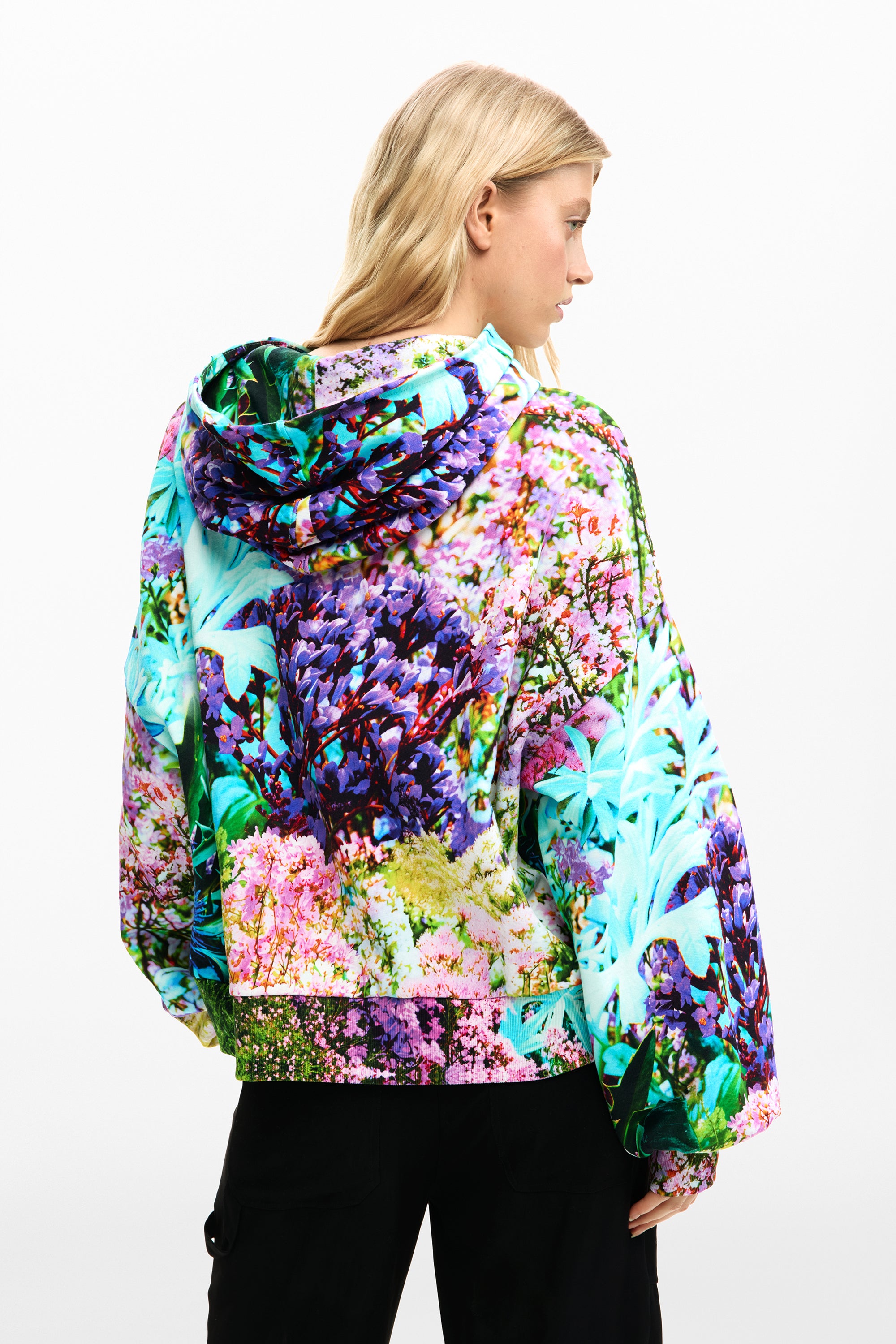 אישה עם ג'קט קפוצ'ון צבעוני בדוגמת פרחים מרובה צבעים, מבט מאחור