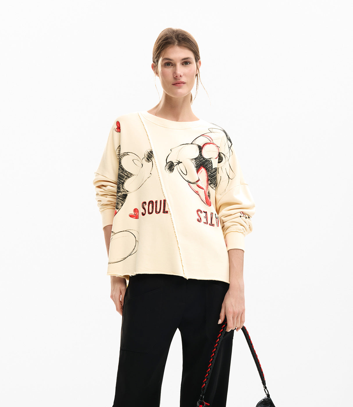 דוגמנית לובשת סווטשירט קרם עם דמויות מצוירות והכיתוב SOUL, מכנסיים שחורים ותיק יד