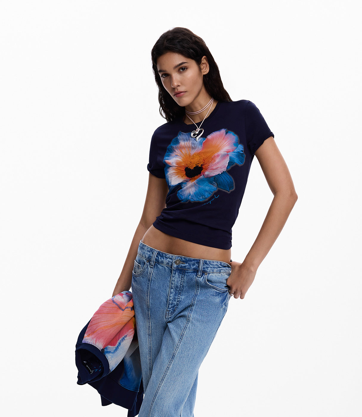 אישה לובשת טי שרט כחולה עם הדפס פרח צבעוני ומחזיקה ג'קט תואם, ג'ינס בגזרת בויפרנד