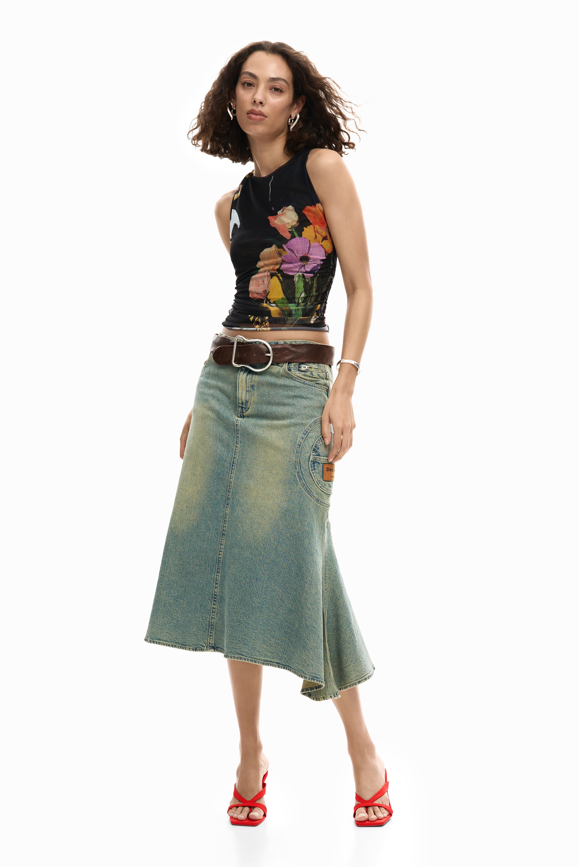 דוגמנית לובשת חצאית ג'ינס ארוכה, חגורה חומה, גופיית פרחים צבעונית ונעלי עקב אדומות