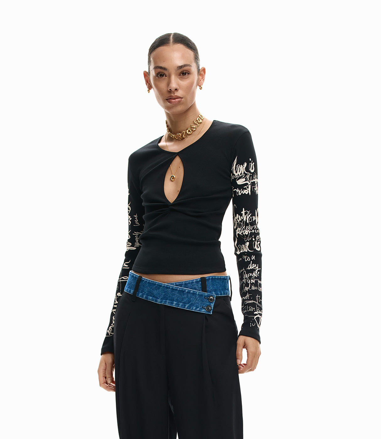 אישה לובשת חולצת שרוול ארוך שחורה עם כיתוב לבן ופתח חזה, מכנסיים שחורים וחגורת ג'ינס
