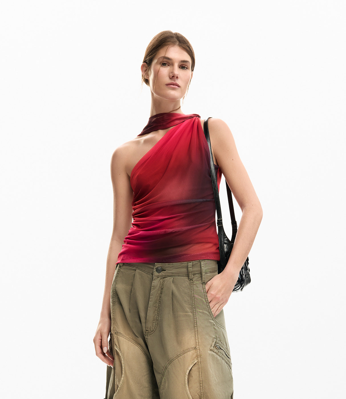 אישה עם גופייה אדומה אסימטרית ומכנסי בד ירוקים אופנתיים, תיק שחור על הכתף