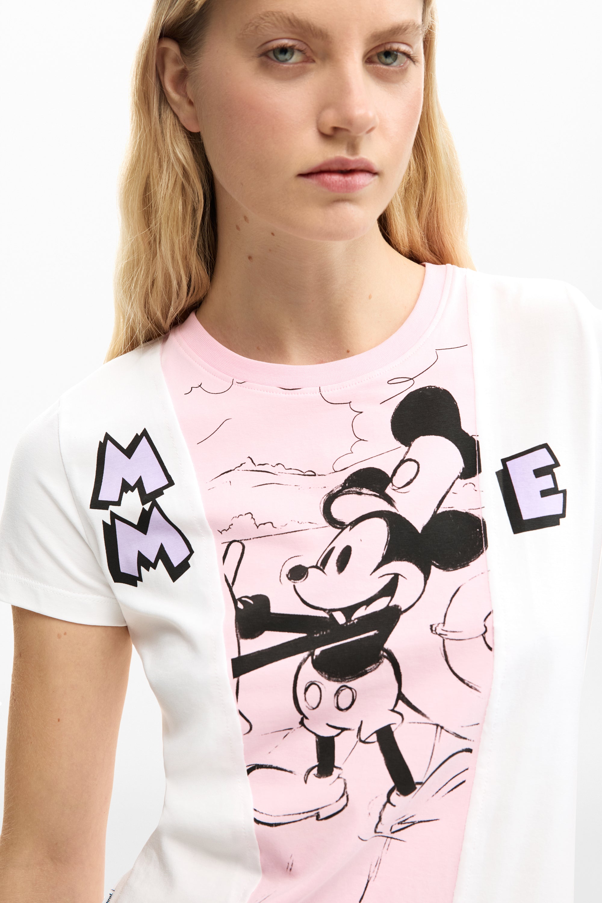 אישה עם חולצת טי קצרה לבנה וורודה עם הדפס דמות מצוירת, אותיות MM ו-E מעוצבות