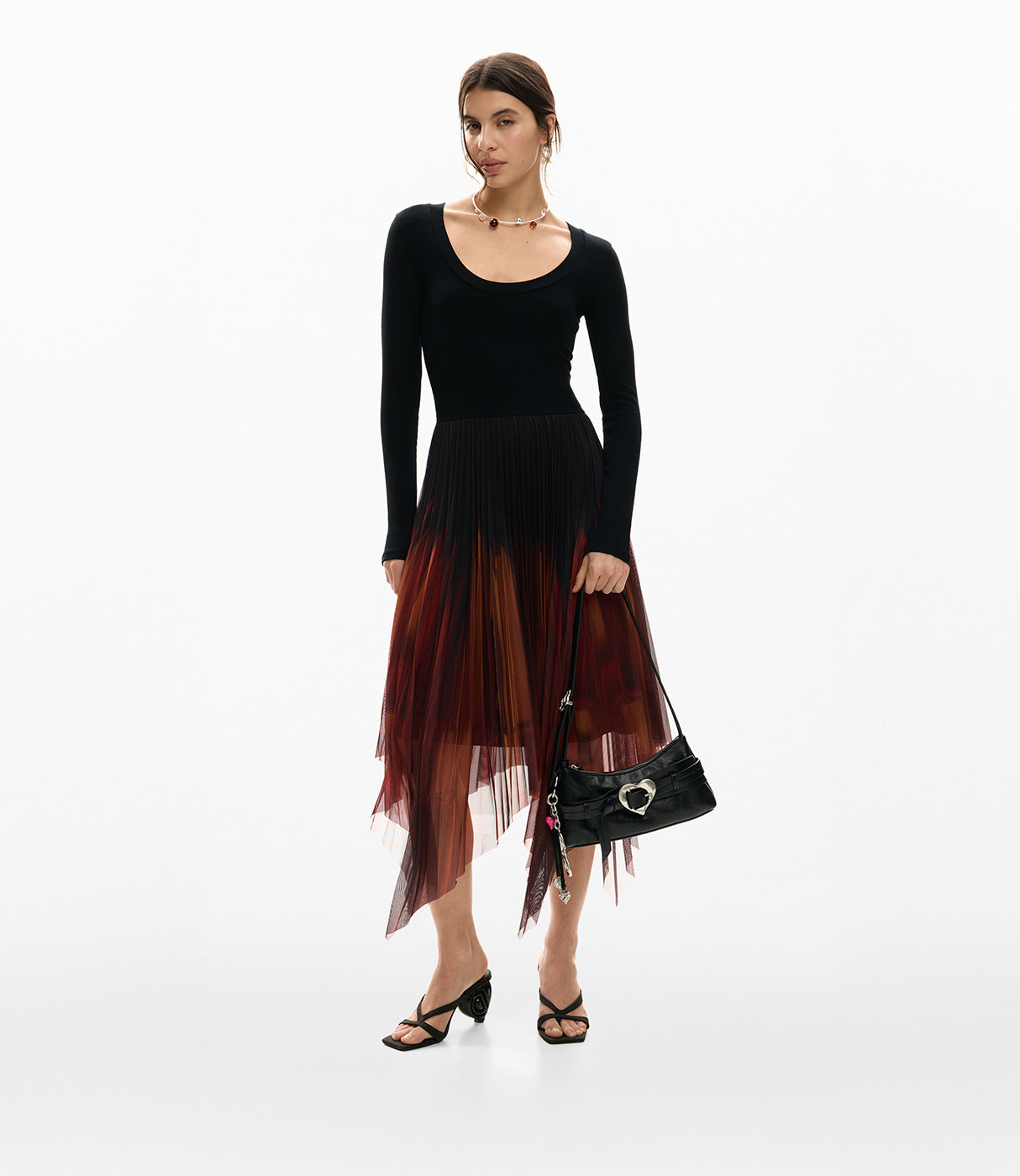 אישה לובשת שמלת ערב עם שרוולים ארוכים בשחור וחצאית פליסה בגווני אדום, מחזיקה תיק צד שחור