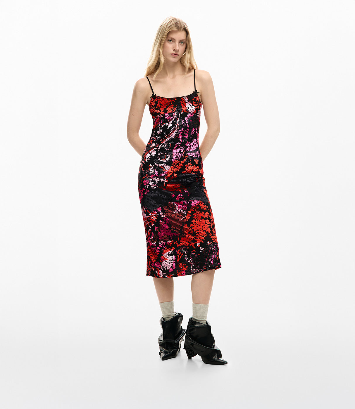 דוגמנית לובשת שמלה מידי פרחונית בצבעים ורוד, אדום ושחור עם כתפיות דקות ונעליים שחורות ייחודיות