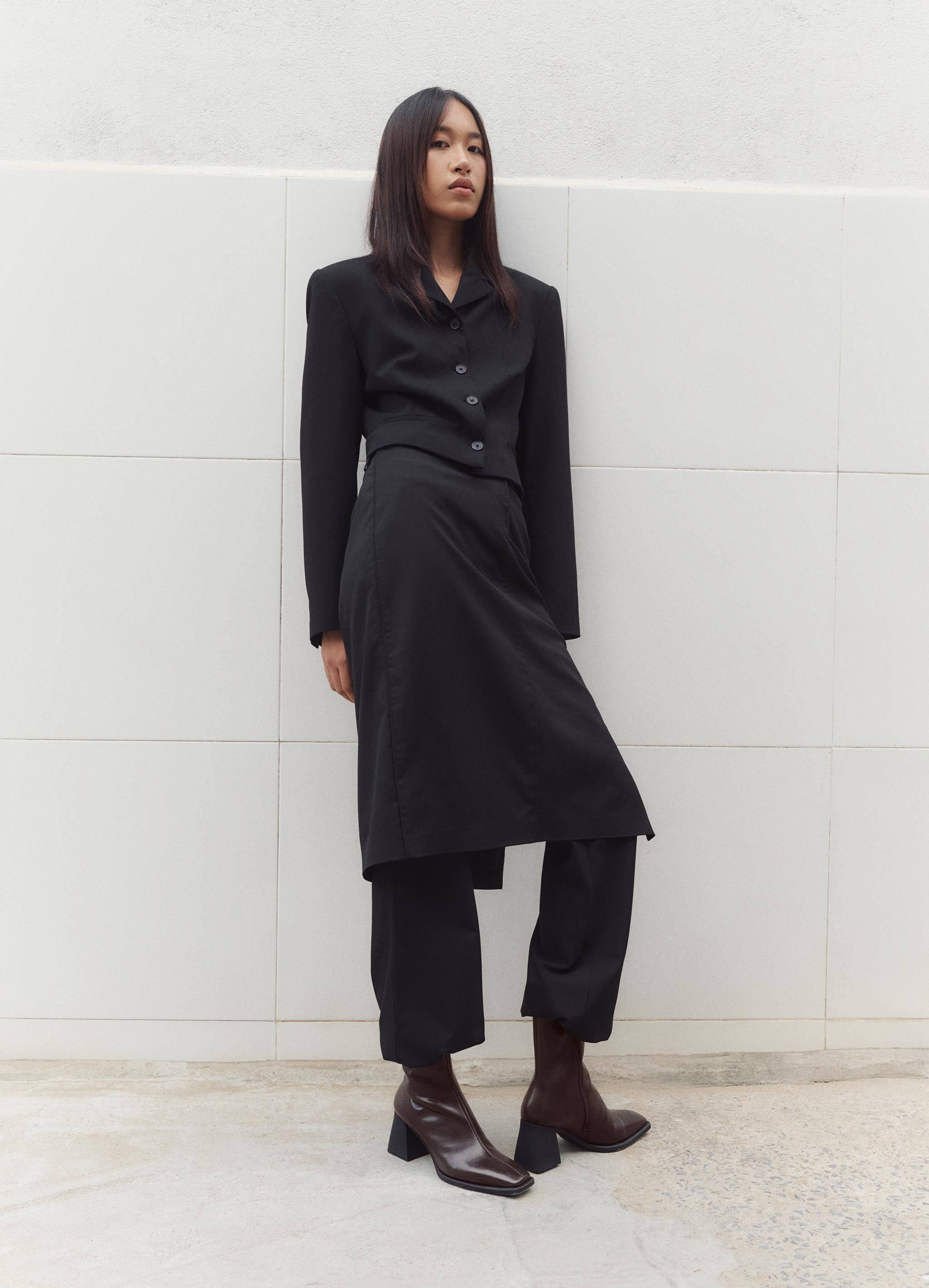 דוגמנית עומדת לבושה חליפת נשים שחורה אלגנטית ונעליים חומות, צולם לקמפיין CHOZEN