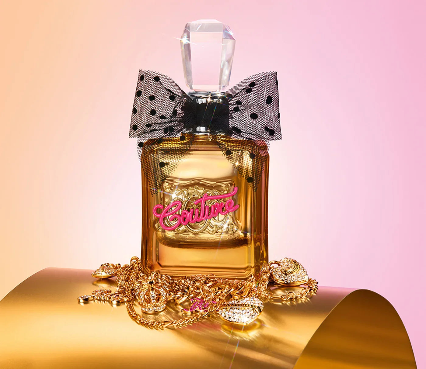 בקבוק בושם יוקרתי עם פקק גבישי, פפיון שחור מנוקד ותכשיטי זהב ברקע ורוד