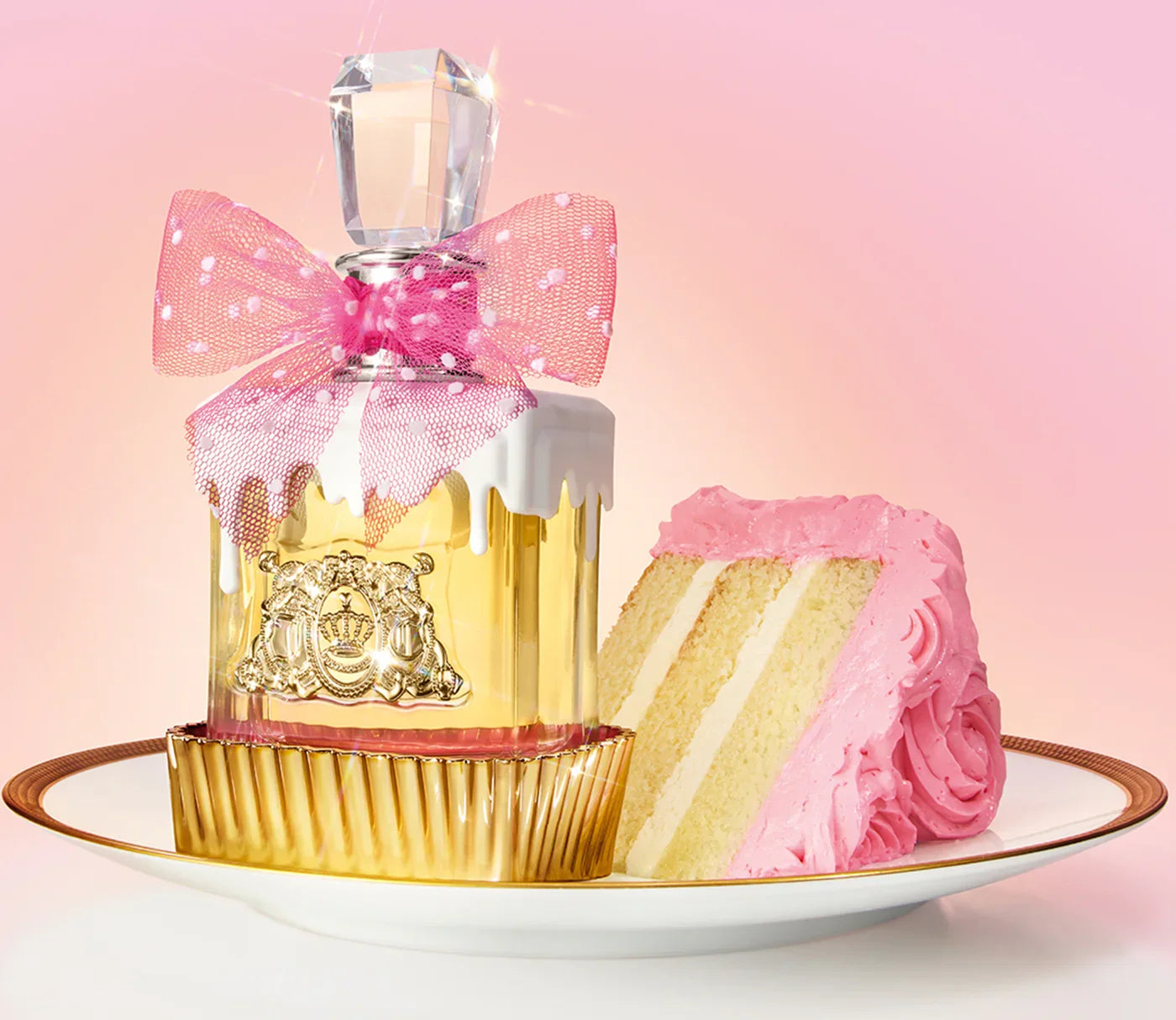 בקבוק בושם מעוצב עם פקק קריסטל, סרט ורוד ועוגת וניל עם קרם ורוד על צלחת, רקע ורוד