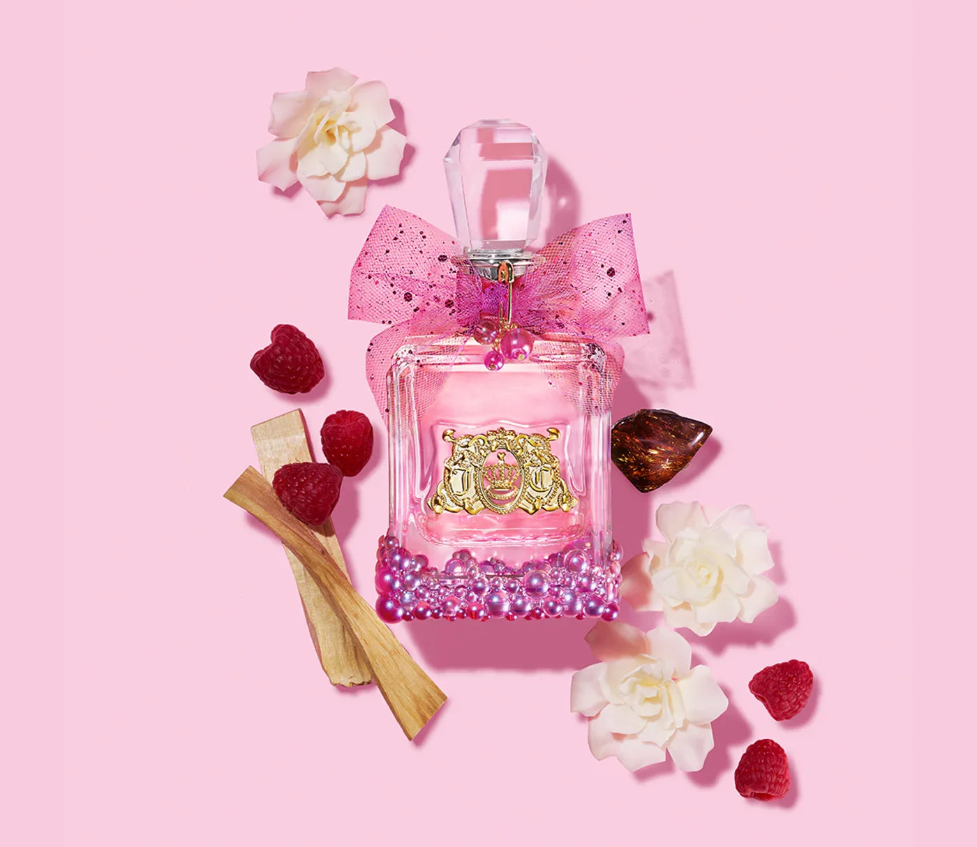 בקבוק בושם ורוד עם פקק קריסטל, סרט קישוט, מוקף פטל, פרחים לבנים ועץ על רקע ורוד