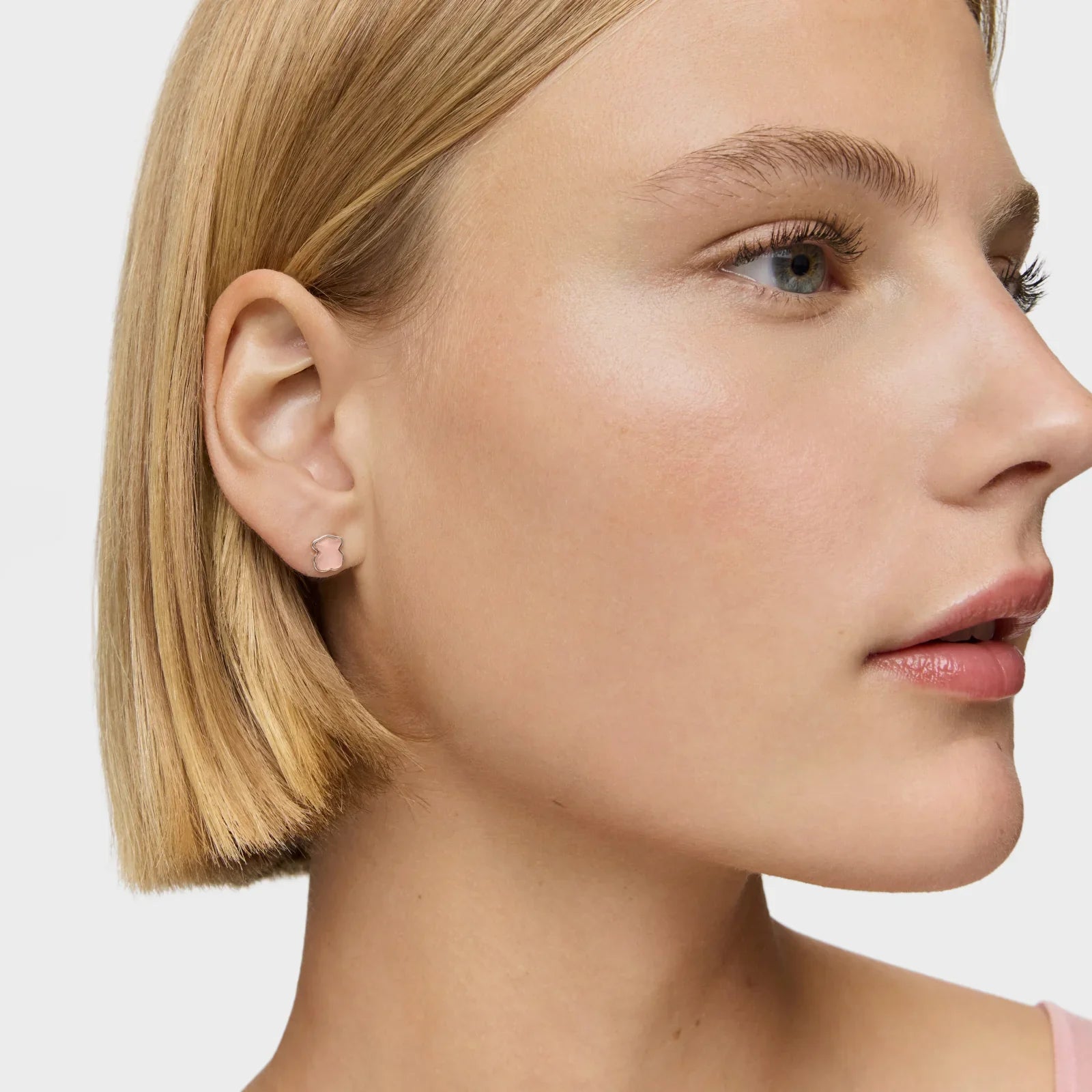 אישה עם שיער בלונד קצר עונדת עגילי סטאד קטנים בצורת דובי בצבע ורוד בוהק